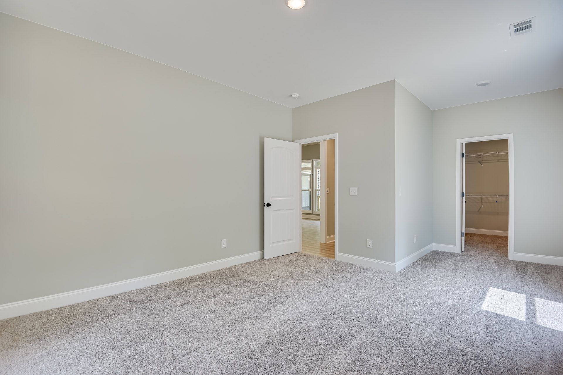 White paneled door with black knob open to a room with light laminate flooring, white plaster walls, and ceiling.