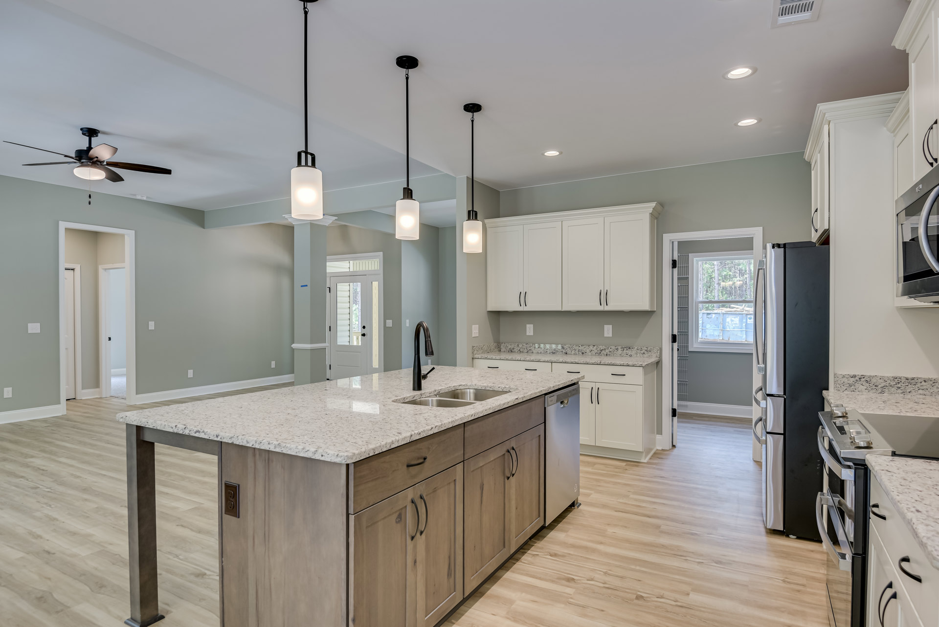 Spacious kitchen featuring a large central island with built-in sink, white cabinetry with black handles, oversized stainless steel refrigerator, pendant lighting, tiled