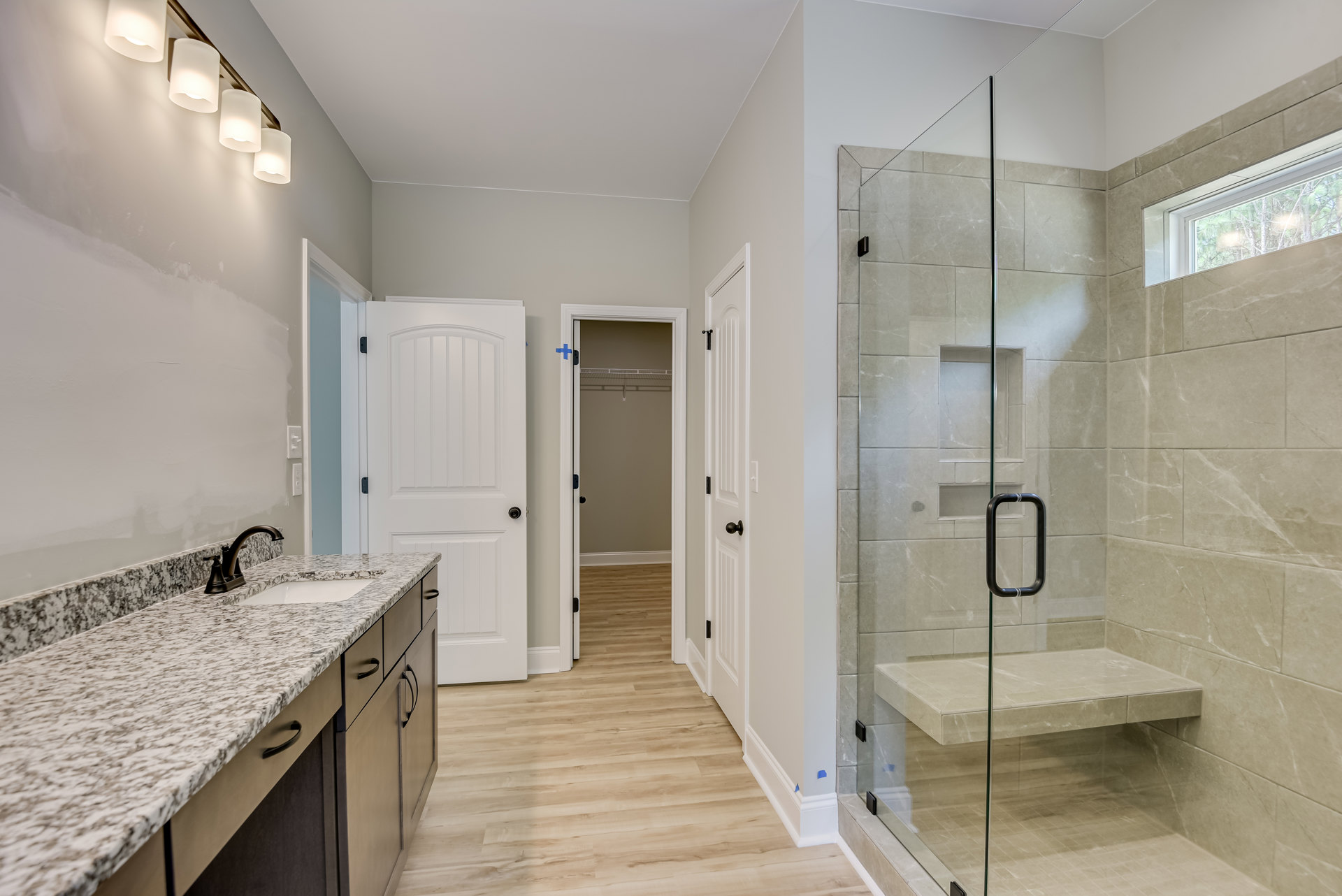 Bathroom featuring a glass-enclosed shower with built-in bench, marble countertop with black handle, modern sink and faucet, white door, and contemporary light fixtures.