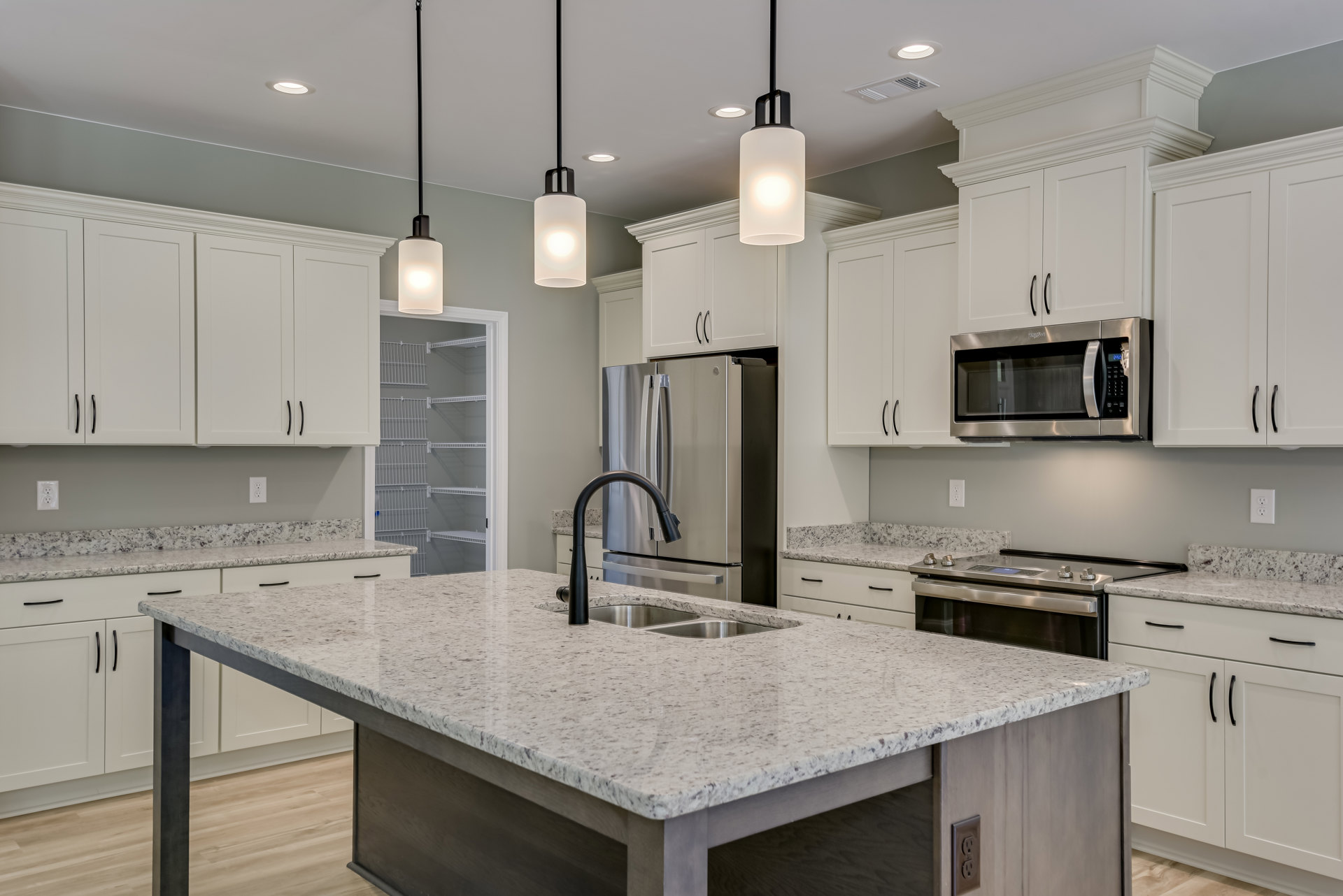 Spacious kitchen featuring a large central island with stone countertop, stainless steel refrigerator, built-in microwave with open door, undermount sink with chrome faucet, tile