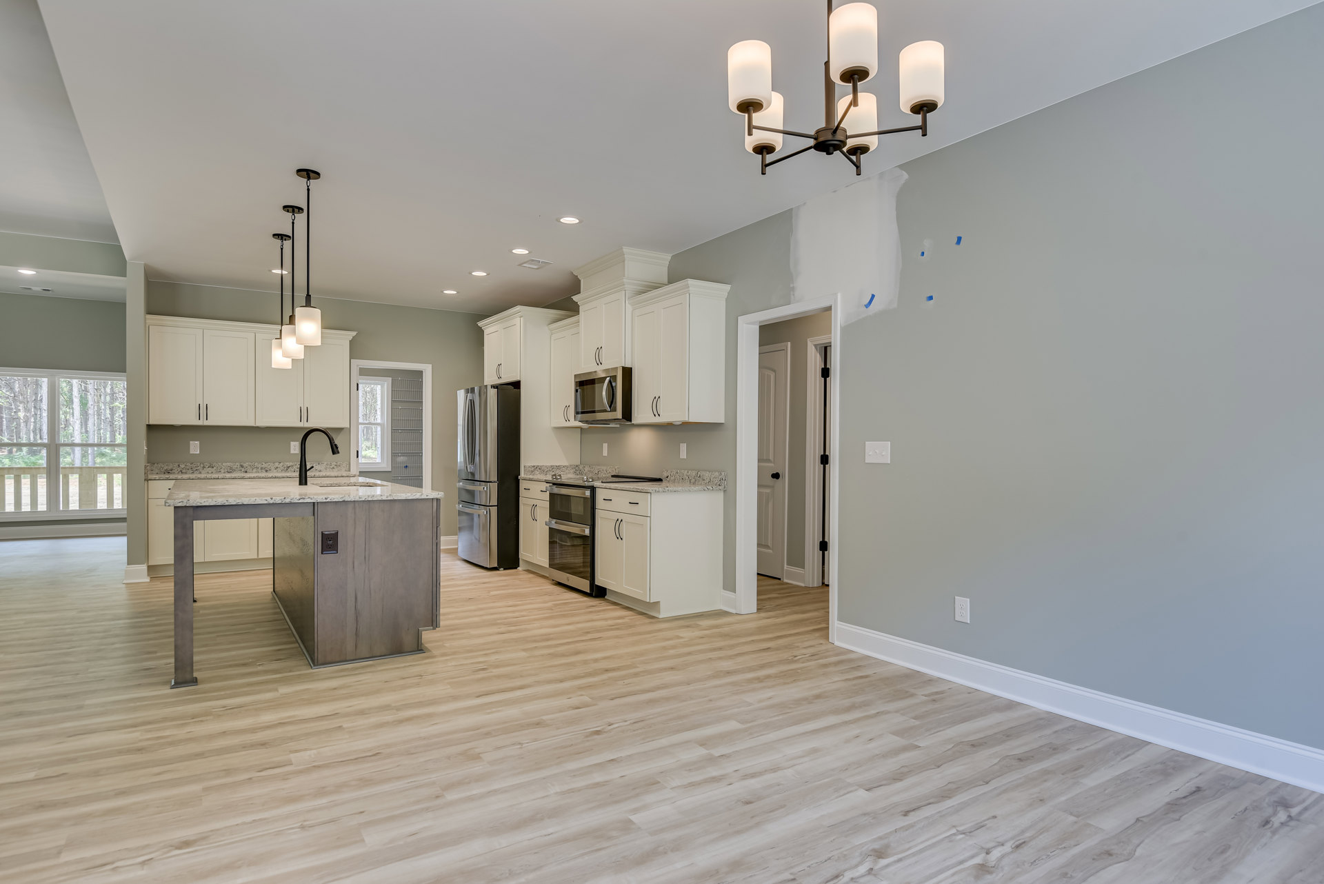 Open kitchen and dining area featuring wood flooring, white cabinetry, stainless steel refrigerator, kitchen island with black pendant light, built-in microwave, and chandelier