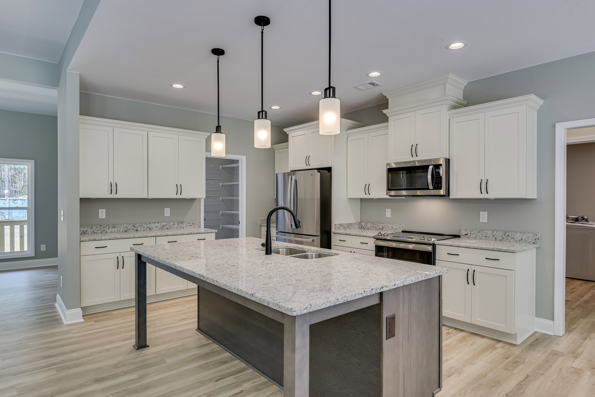 Spacious kitchen featuring a large central island with built-in sink and stove, white shaker cabinets, stainless steel microwave, pendant light fixture, tile backsplash, and window