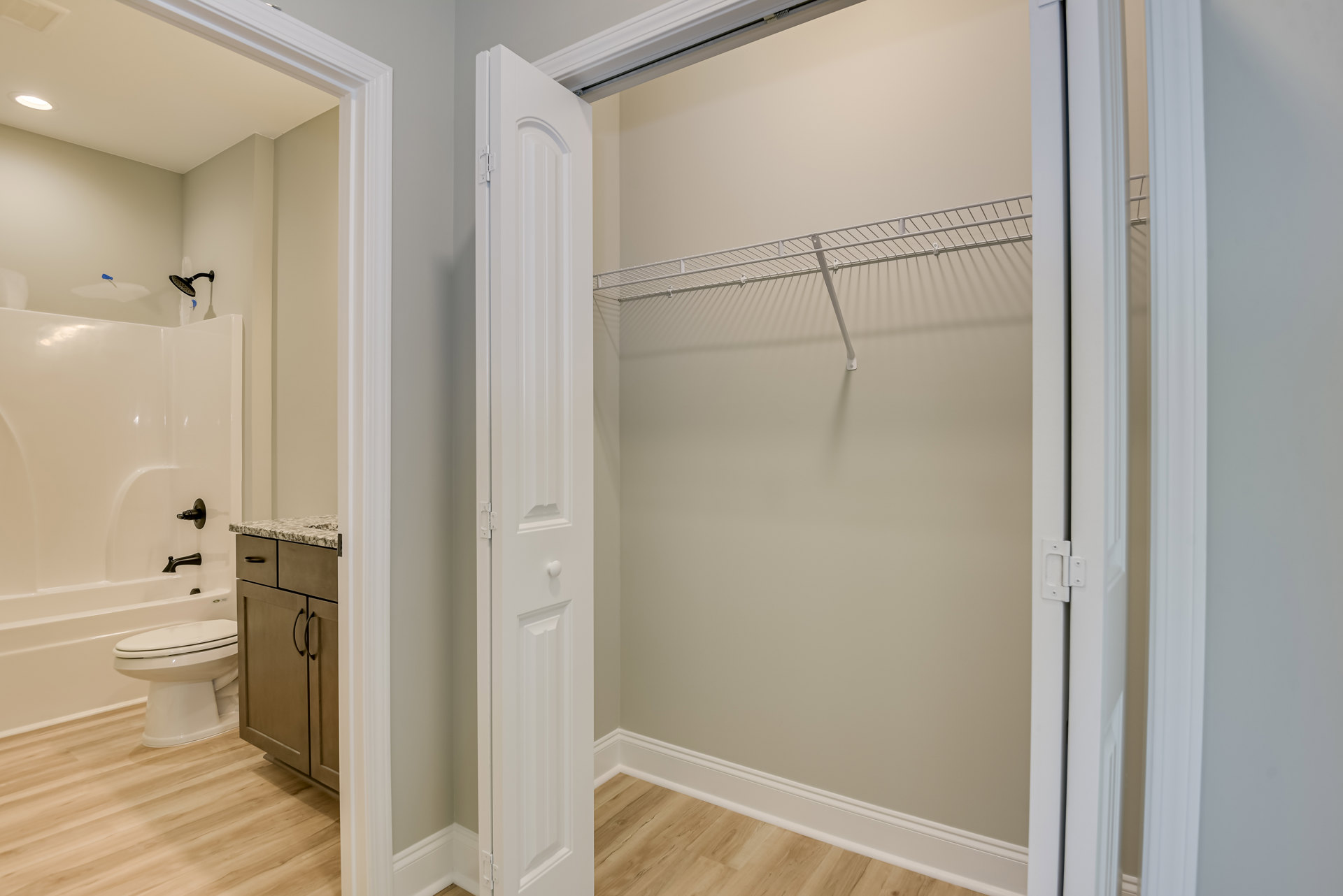 Walk-in closet with built-in white shelf, adjacent bathroom featuring white toilet, white bathtub with black faucet, shower curtain, and tile flooring