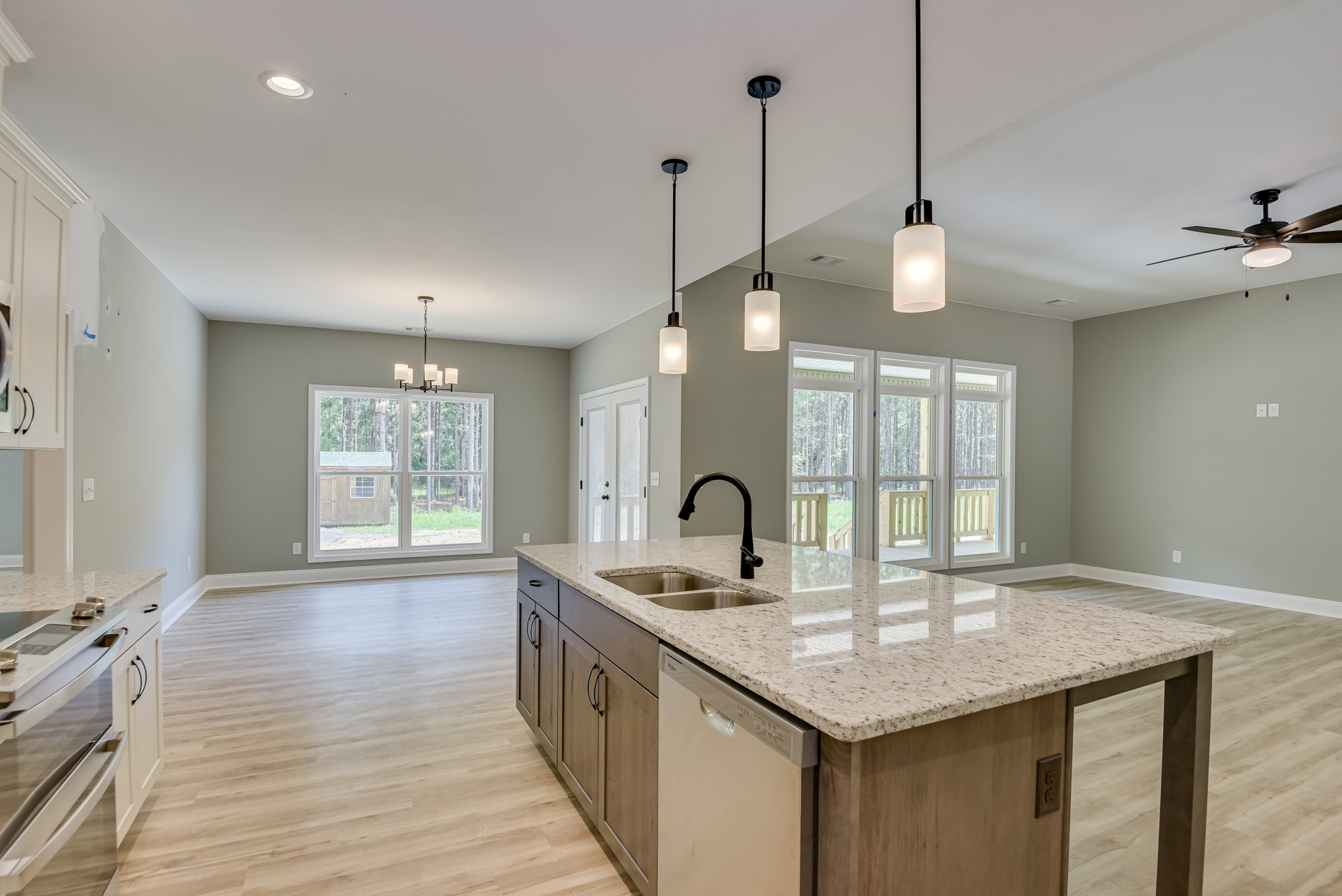 Spacious kitchen featuring a large white island with quartz countertop, undermount sink, built-in dishwasher, tile backsplash, white cabinetry, pendant light fixtures, and windows
