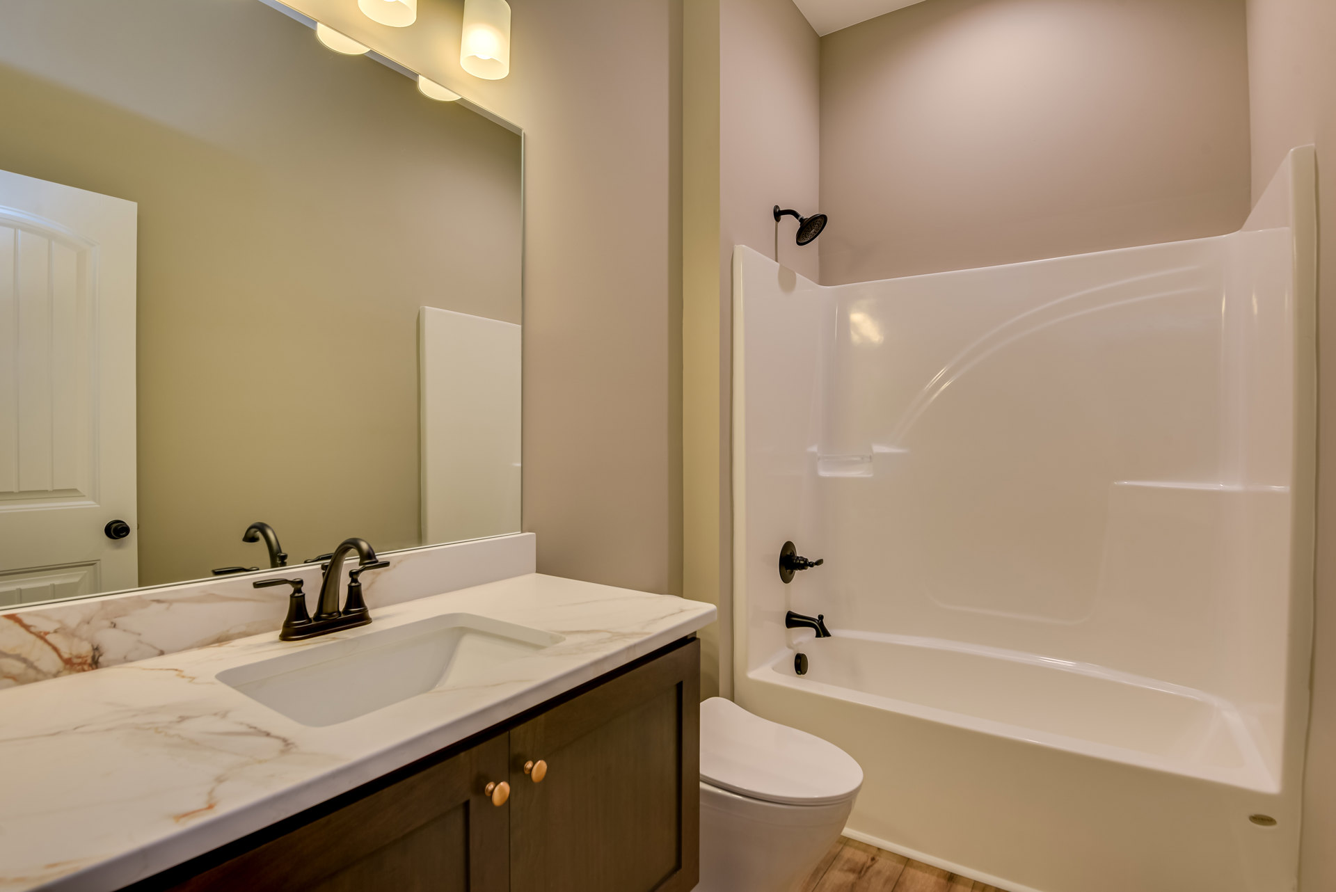 Modern bathroom featuring a white bathtub, toilet with seat down, rectangular sink with chrome faucet, large mirror, and light-colored tile walls