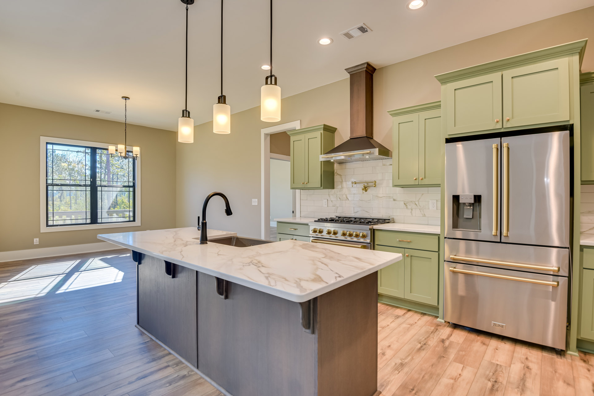 Marble kitchen island with built-in sink, stainless steel refrigerator with water dispenser, white cabinetry, tile backsplash, pendant light fixture illuminated, window overlooking