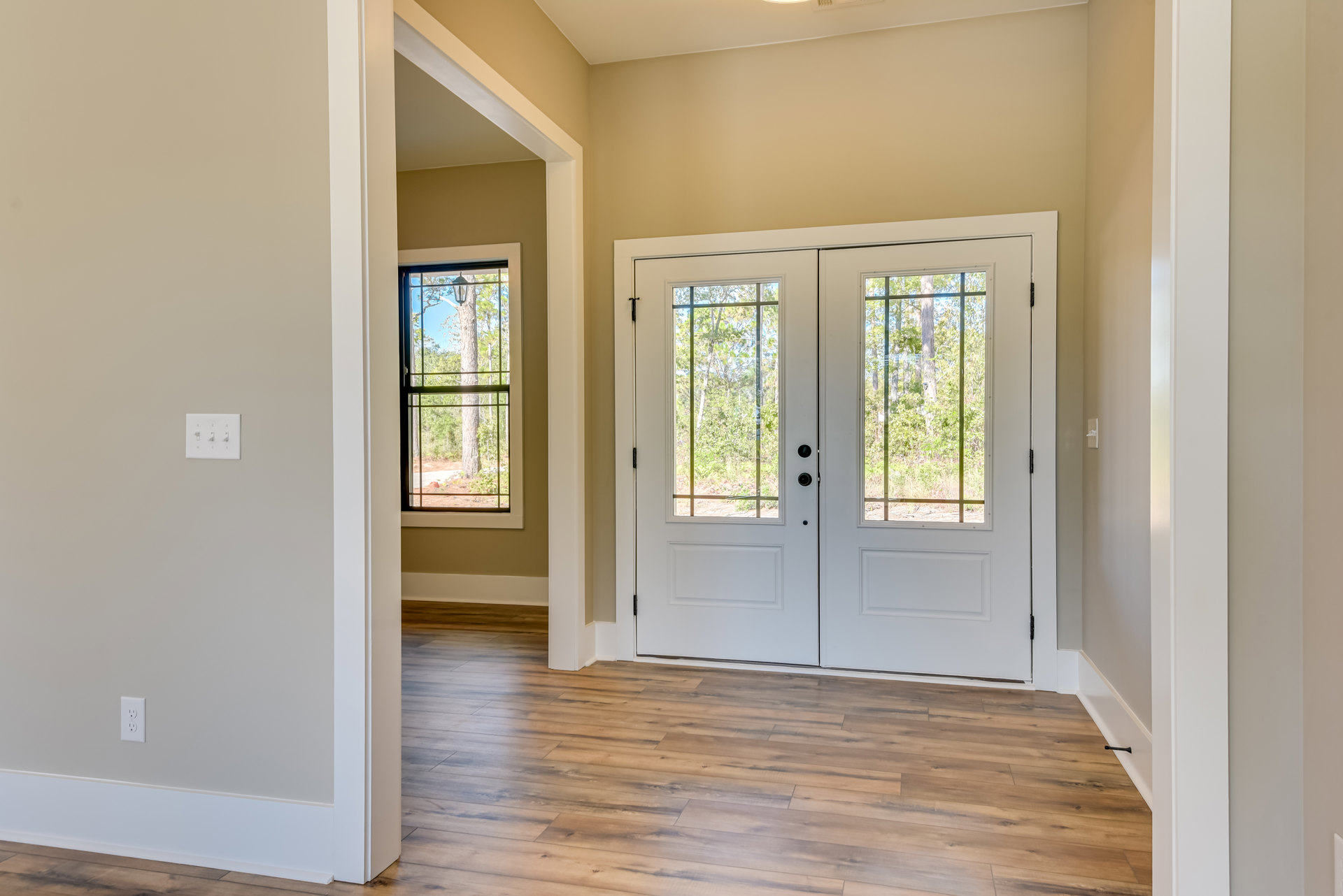 White double doors with glass panes, wood laminate flooring, white walls, three-switch light fixture, window showing trees outside