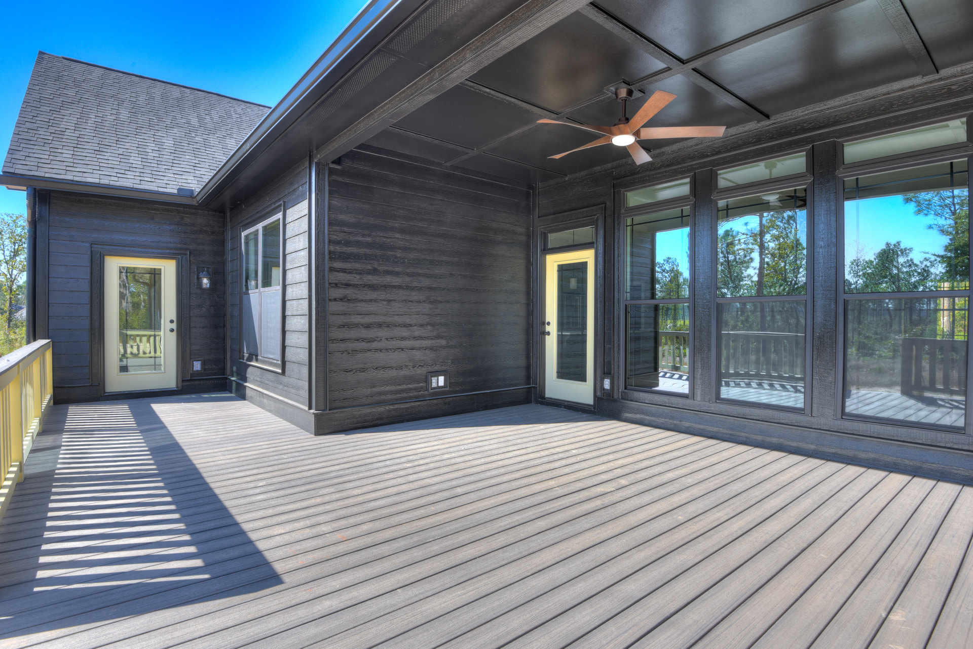 Wooden deck with black ceiling, two ceiling fans with lights, glass door and window leading inside, shaded outdoor area