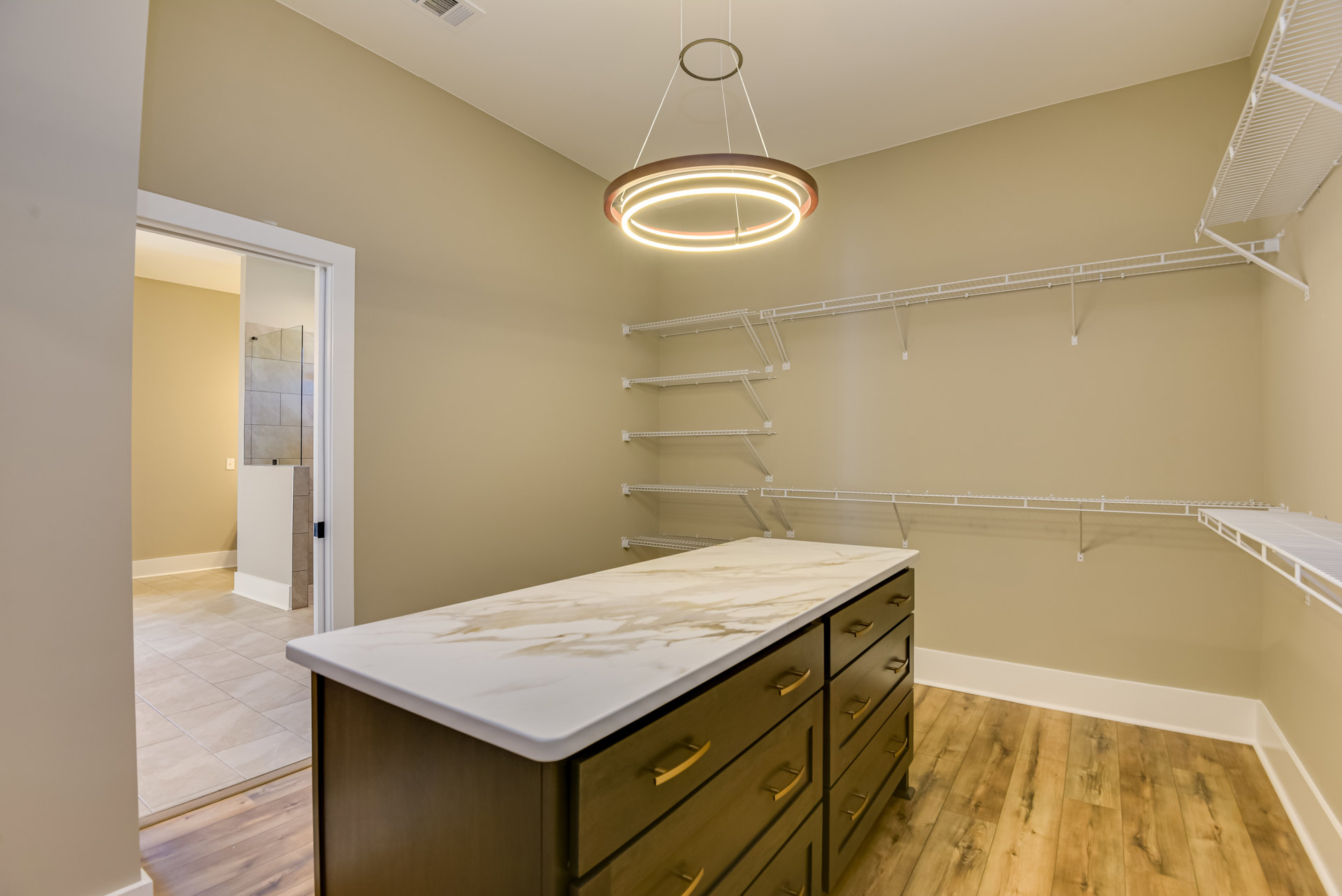 Spacious walk-in closet featuring a central marble island with drawers, white shelving along the walls, and built-in cabinetry.