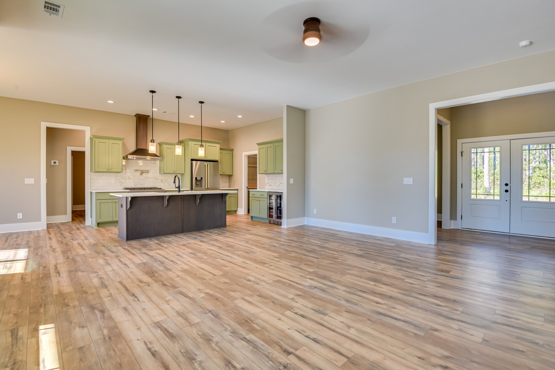Spacious kitchen with wood flooring, white cabinetry, stone countertops, stainless steel faucet, glass double doors, and a white door overlooking trees