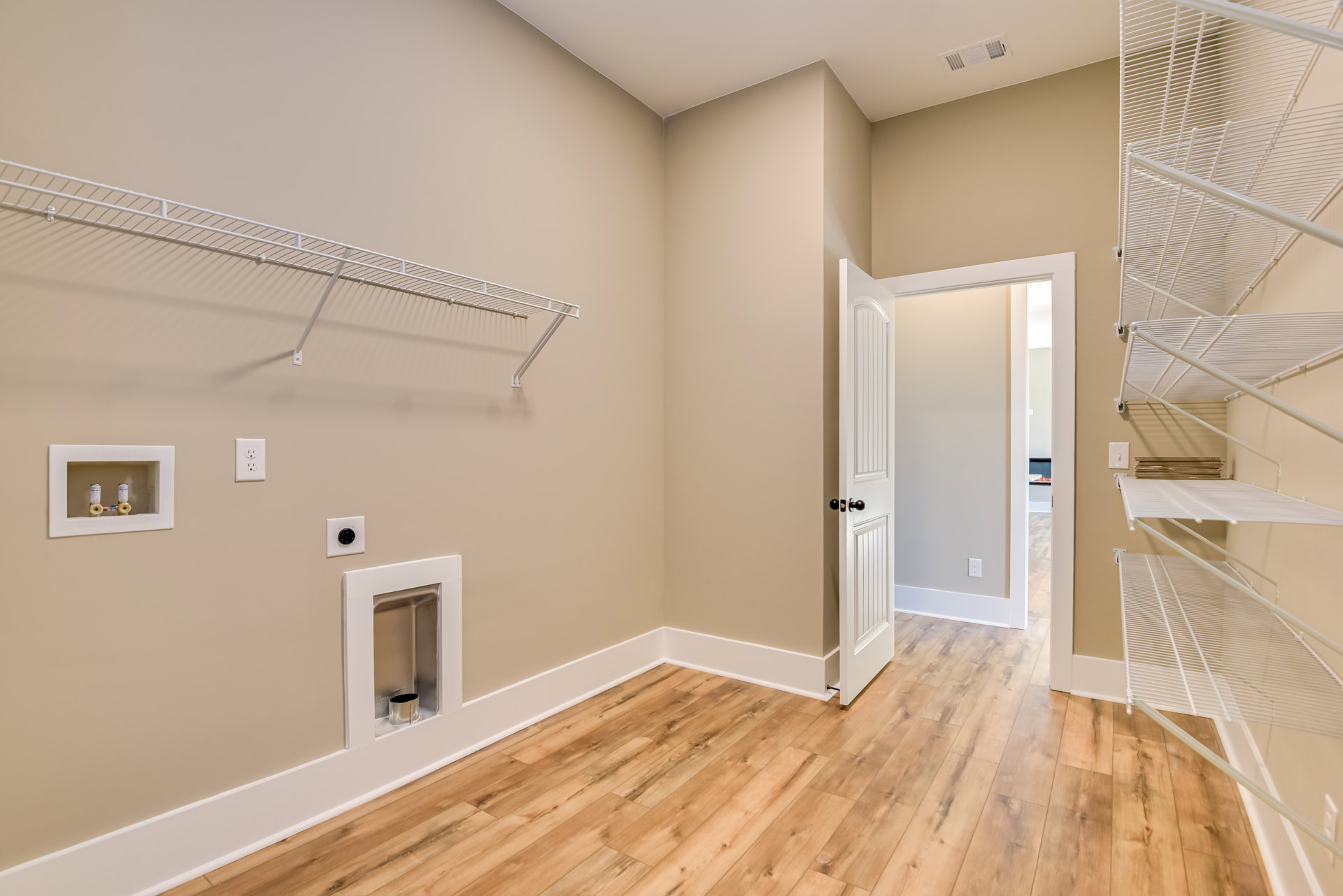 Wood flooring in a bright room featuring a white door, white wall shelves, and a metal container inset into the wall.