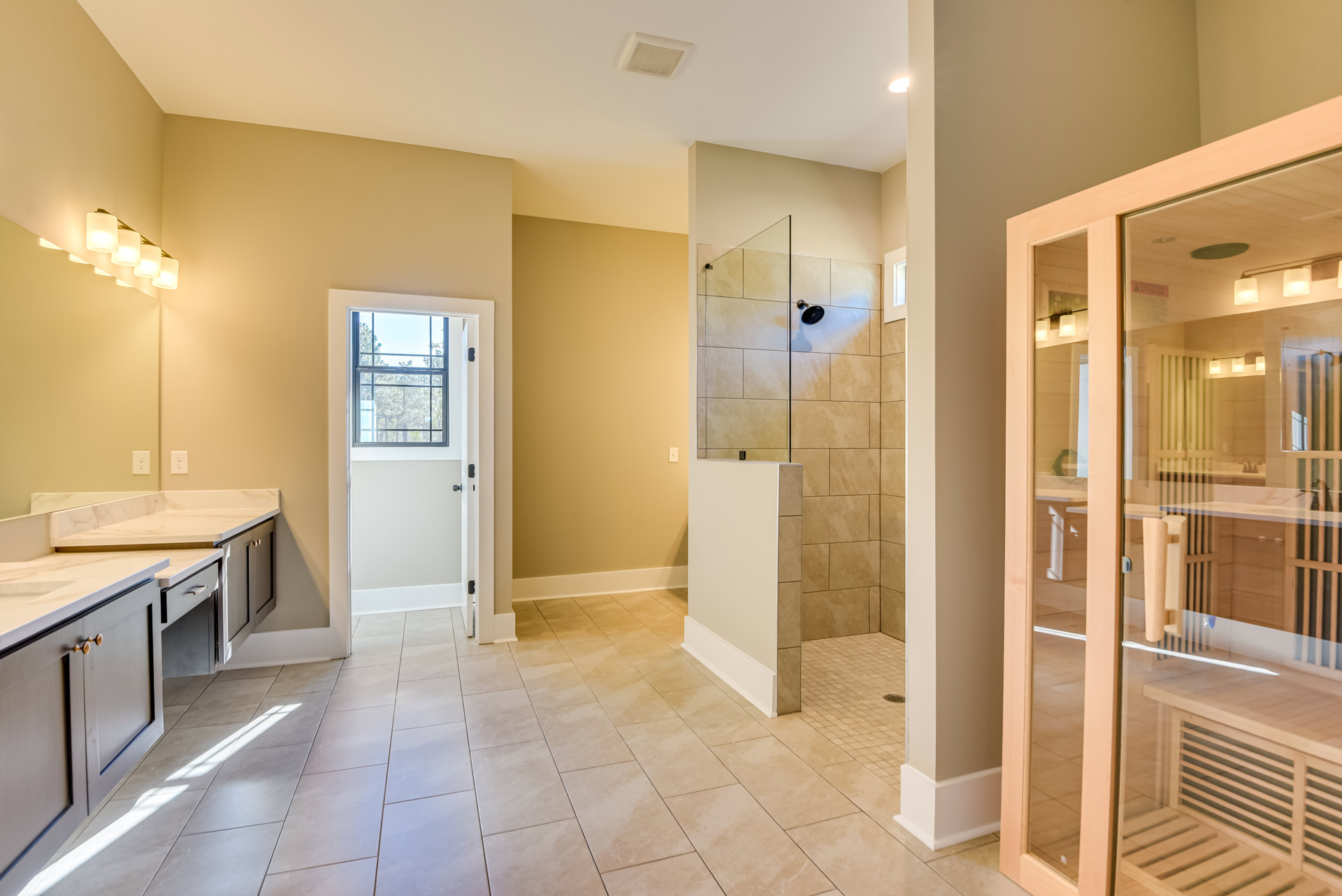 Modern bathroom featuring a glass-enclosed shower, white sink with stone countertop, wood cabinetry, tiled floor, door with frosted window, large window overlooking trees