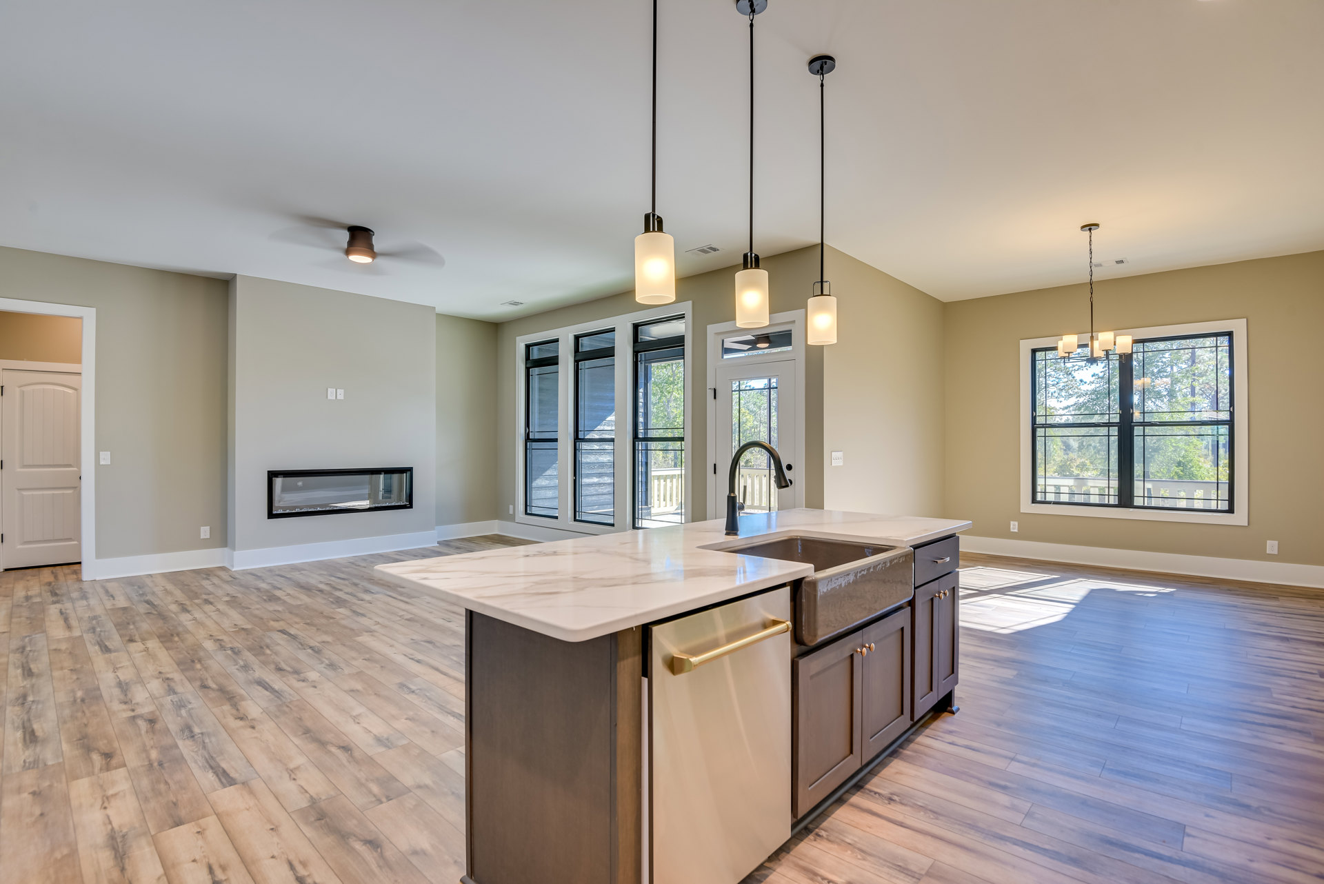 Open kitchen featuring a central island with sink, stone fireplace in the middle, white cabinetry, light wood flooring, modern light fixtures, and large windows with outdoor