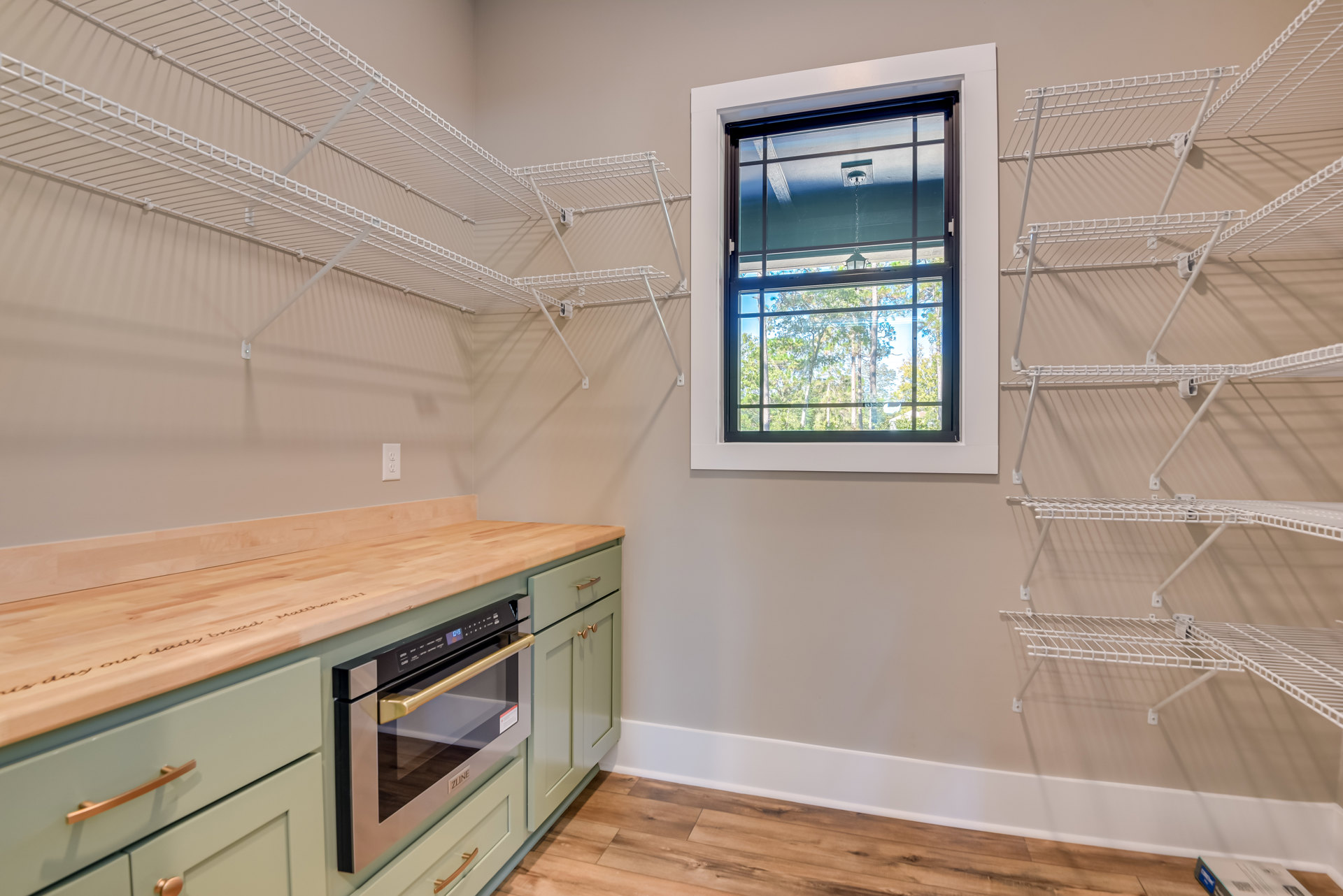 Modern kitchen with plywood cabinetry, open shelves, large window overlooking trees, built-in microwave, and light-colored countertops.