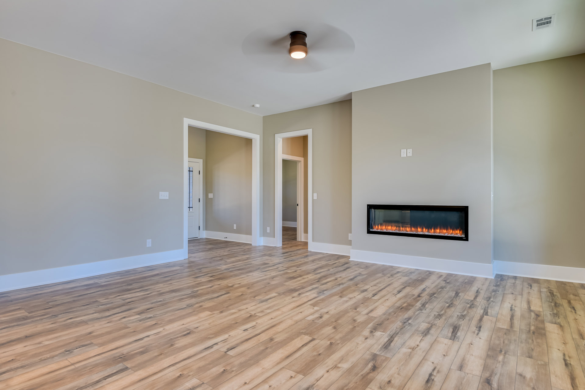 Living room with white walls, hardwood floors, built-in fireplace with fire burning, glass door with white frame, wall vent, and ceiling light fixture.