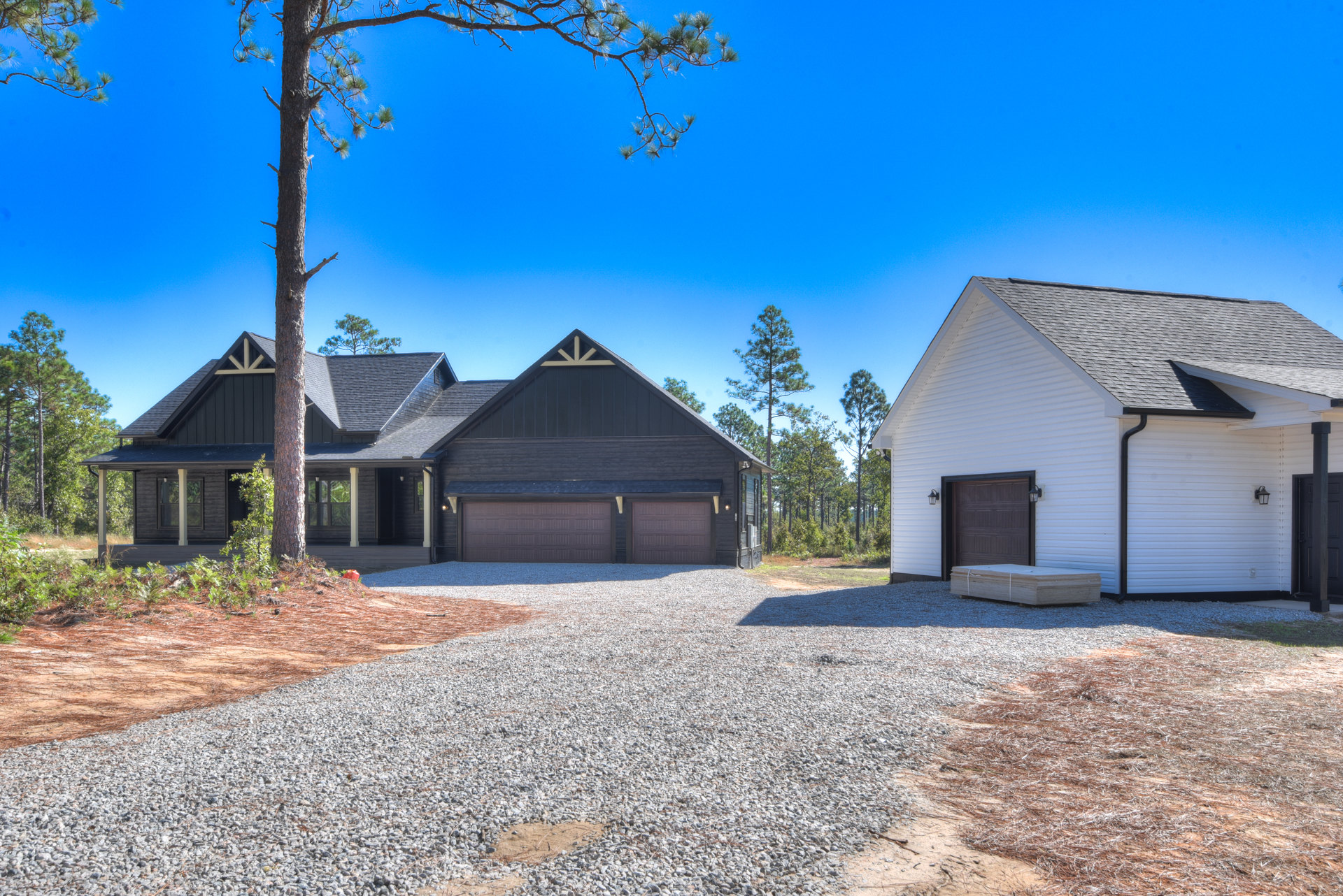 White house with two-car garage, gravel driveway, large leafy tree in front yard, gray roof, and blue sky