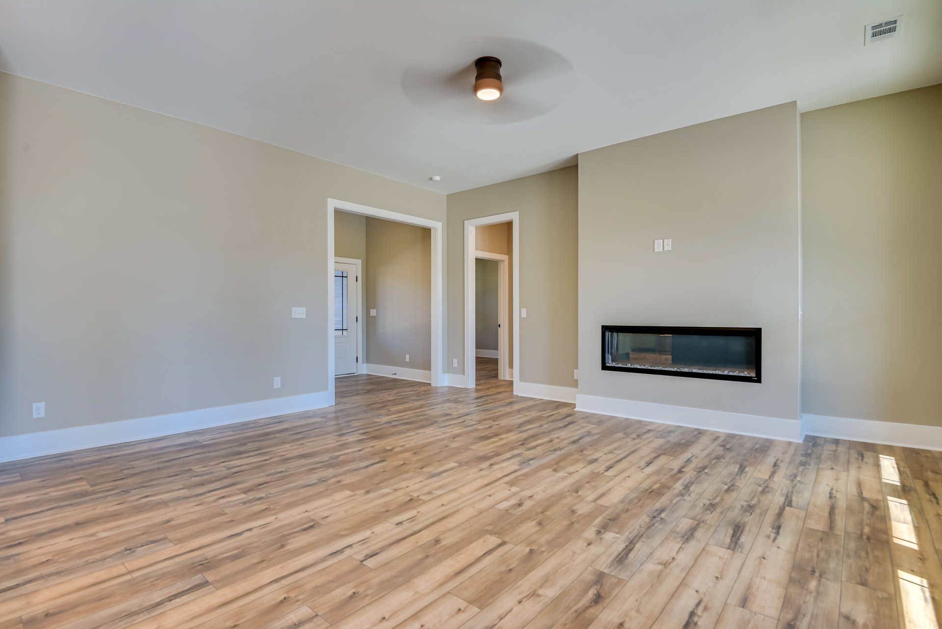 Living room with white walls, wood flooring, black-framed fireplace, white door with black handle, ceiling vent, and recessed lighting.