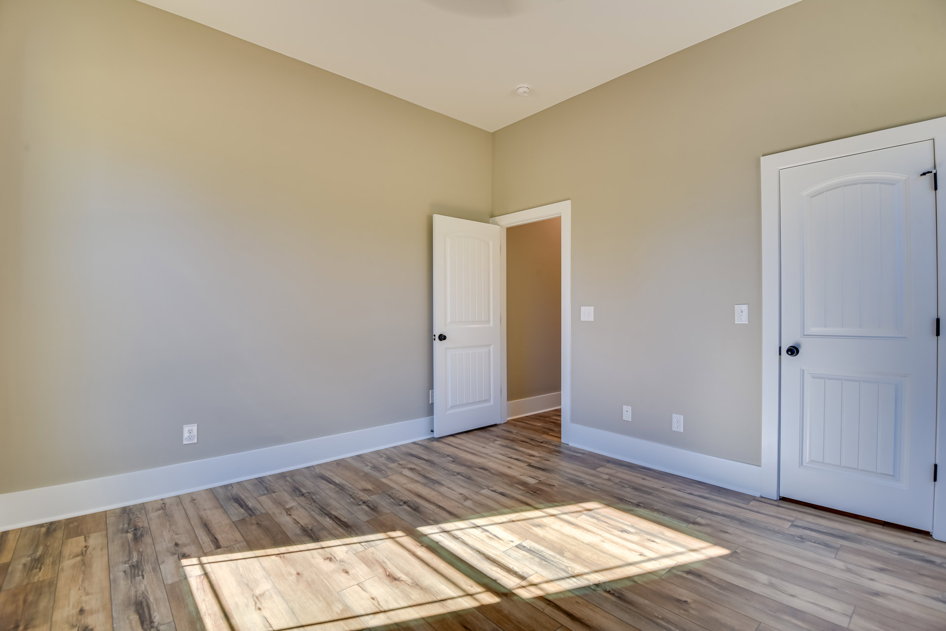 Open white door with black knob leading into a room with hardwood flooring illuminated by sunlight.