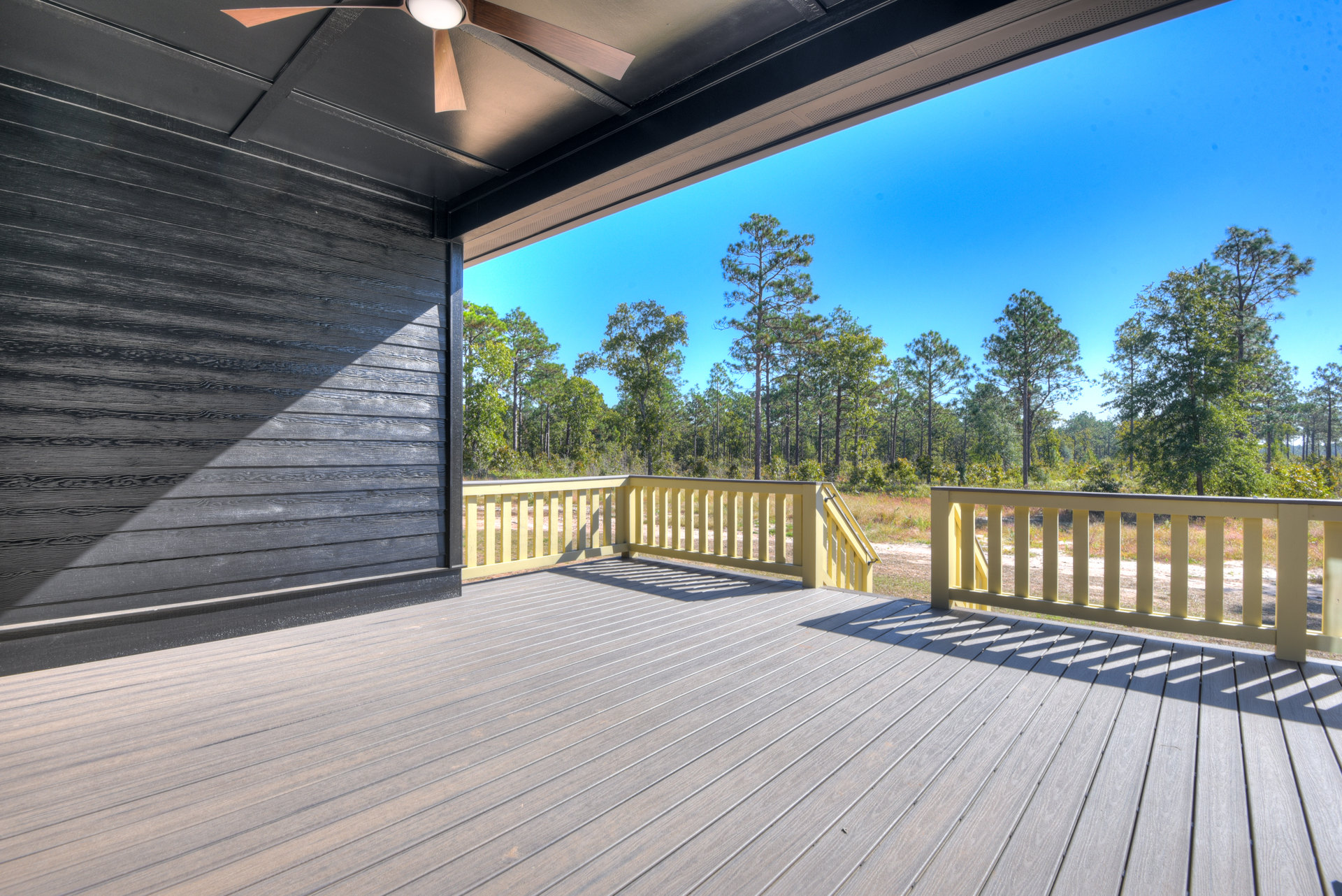 Deck with composite flooring, yellow railing, ceiling fan, overlooking trees and open field