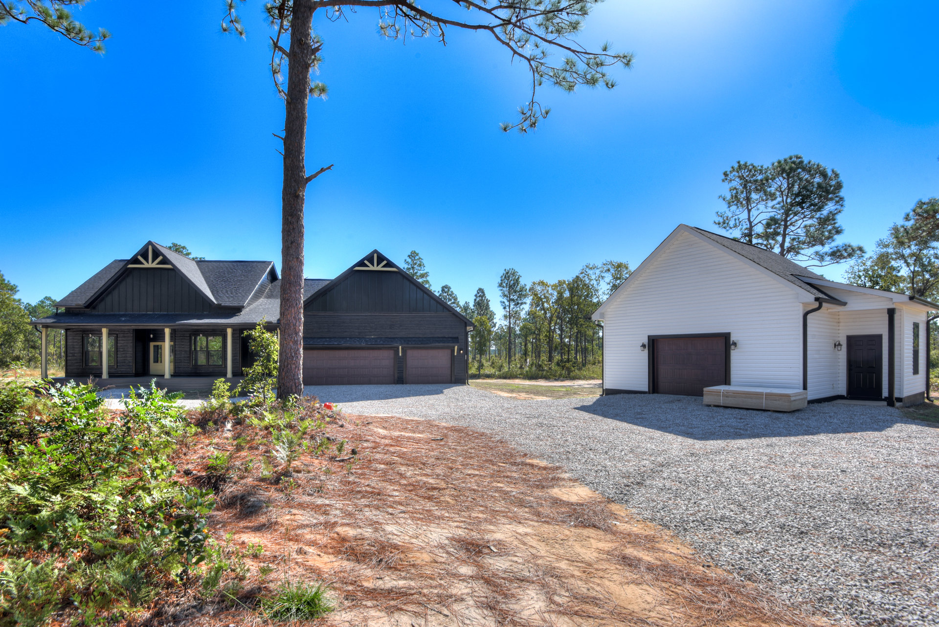 White two-story house with attached garage, concrete driveway, large leafy tree in front yard, man standing near garage door, blue sky overhead