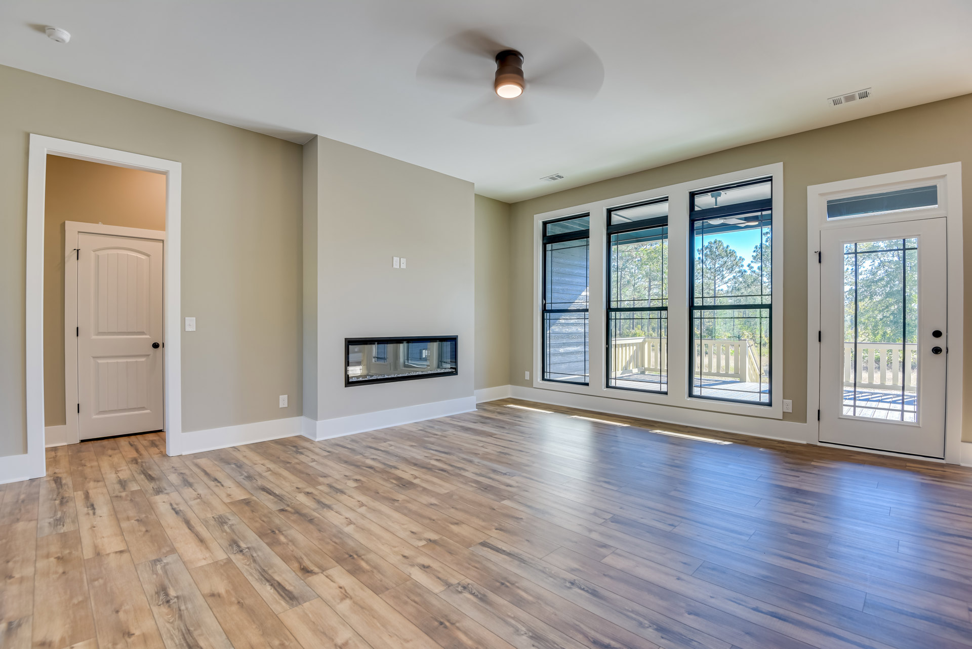 Wood floor room with black-framed window, white door with black knob, ceiling fan, and glass-paneled door; close-up of light fixture; trees visible outside window