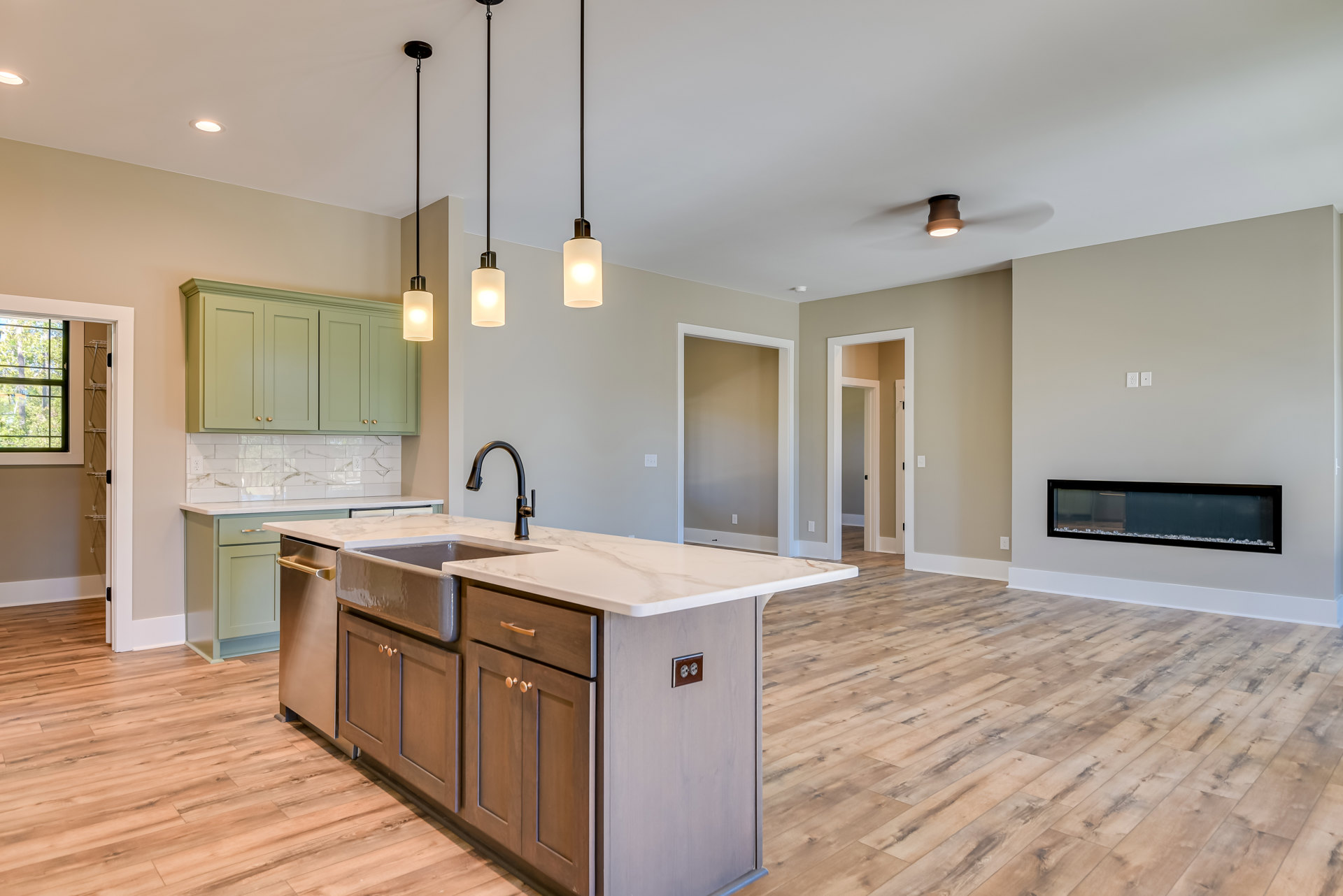 Open kitchen with stainless steel sink, wood plank flooring, white cabinetry, stone countertops, tile backsplash, and large window overlooking trees