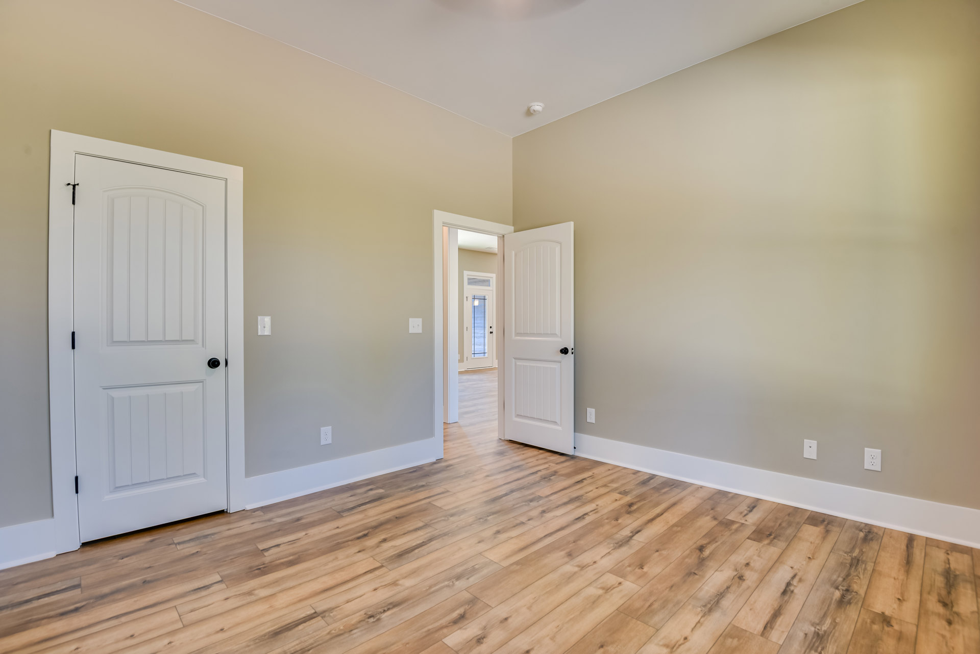 Wood flooring in a room with two white doors featuring black knobs, white walls, and a door with a window.