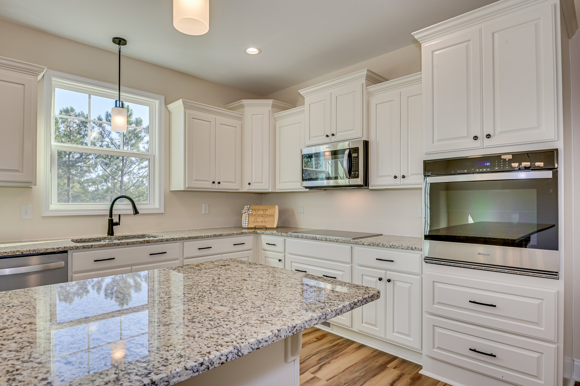 White kitchen cabinets with granite countertops, stainless steel microwave above stove, tile backsplash, window reflecting light onto polished counter, built-in sink, and modern