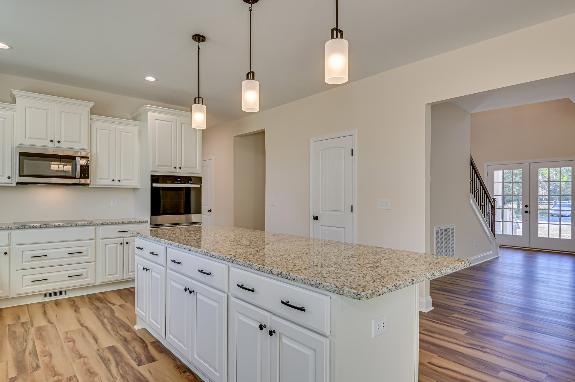 White cabinetry and marble countertops in a modern kitchen, stainless steel microwave, metal bar stool, pendant light fixture, glass-paneled door, and staircase visible in the