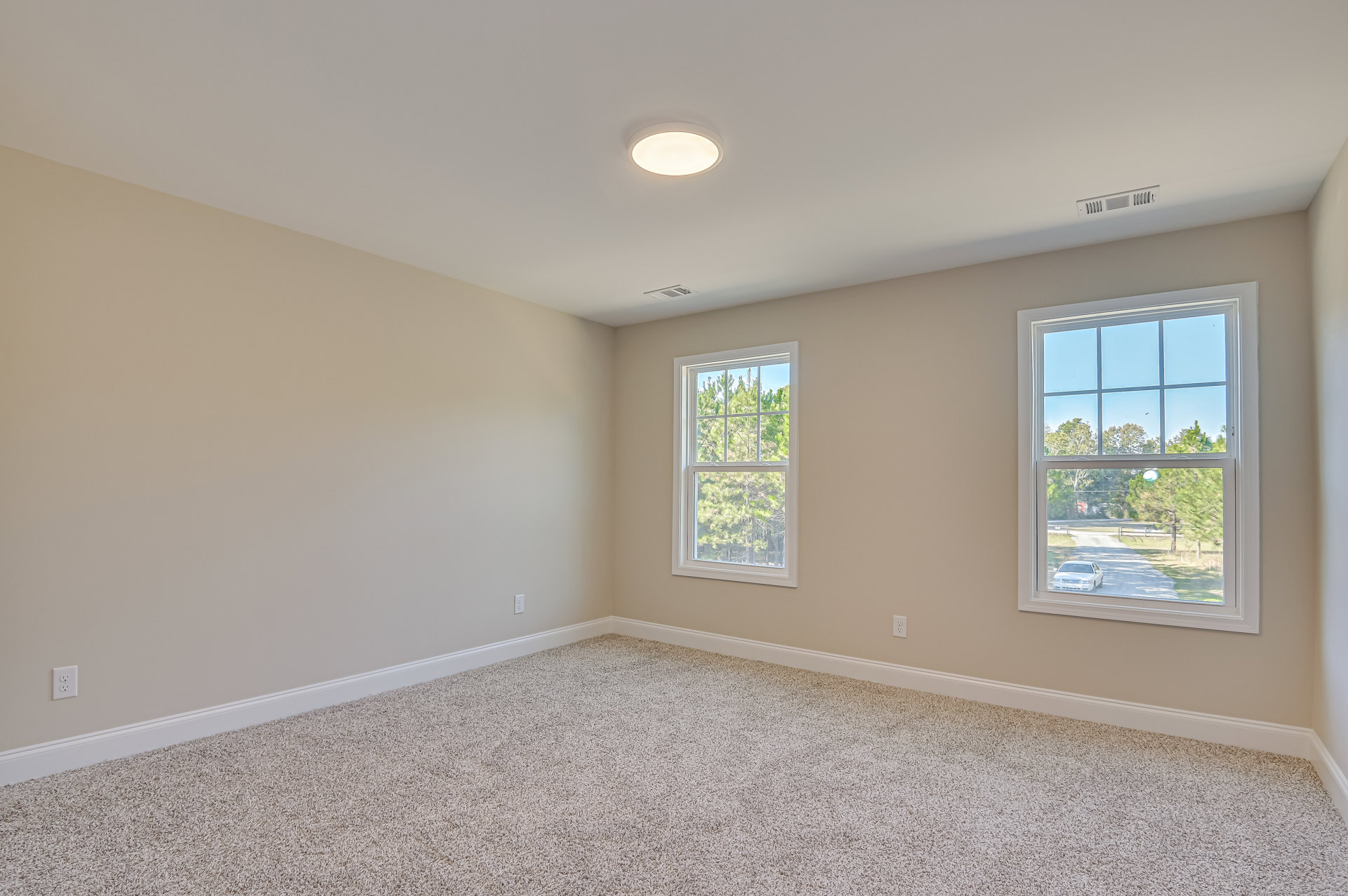 Carpeted room with large windows, white walls, ceiling light fixture, and view of trees and road outside