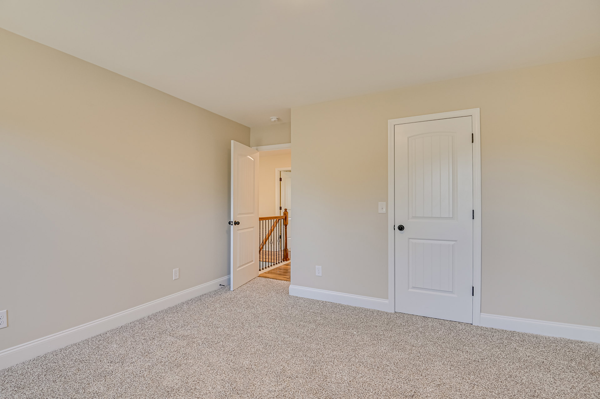 White paneled door with black handle opens to carpeted room, wooden staircase with white railing visible, light-colored walls and crown molding.