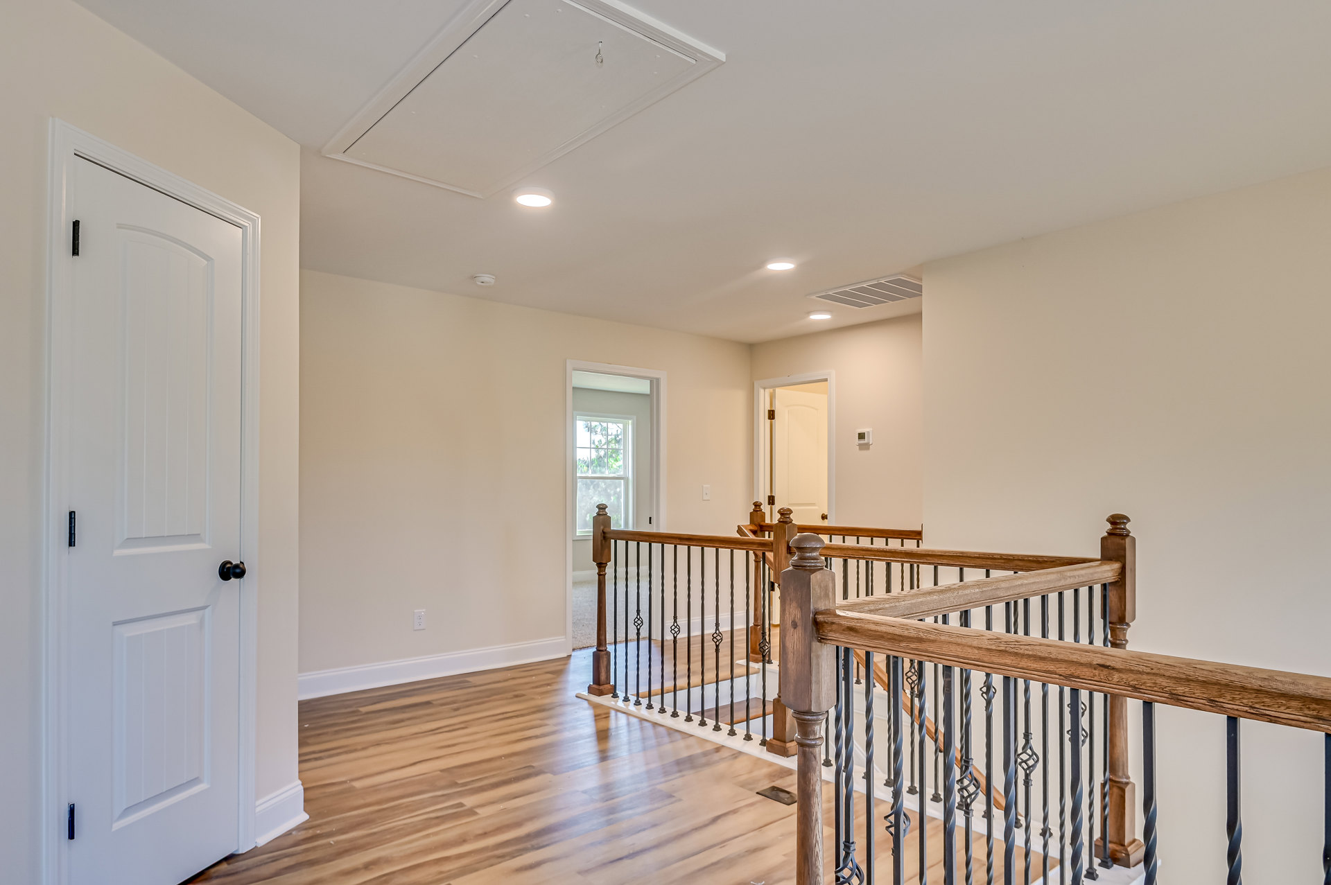 Wood flooring and wooden railing with metal balusters, white door featuring black knob and gold hinge, staircase leading to upper level, neutral walls and ceiling.