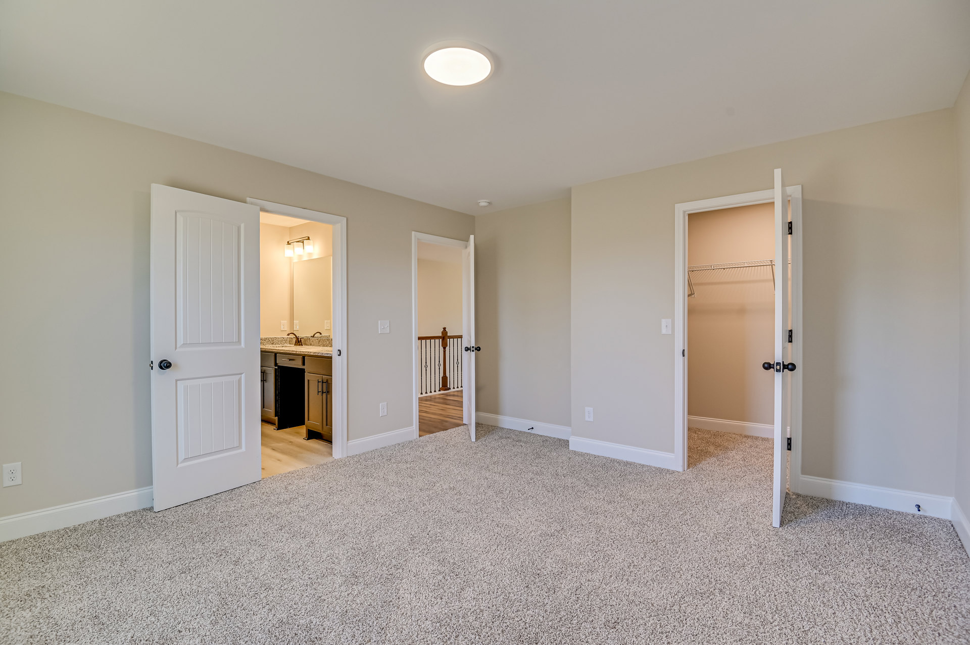 White walls and ceiling, white doors with black knobs, light fixture, white carpeted floor, small table, simple molding