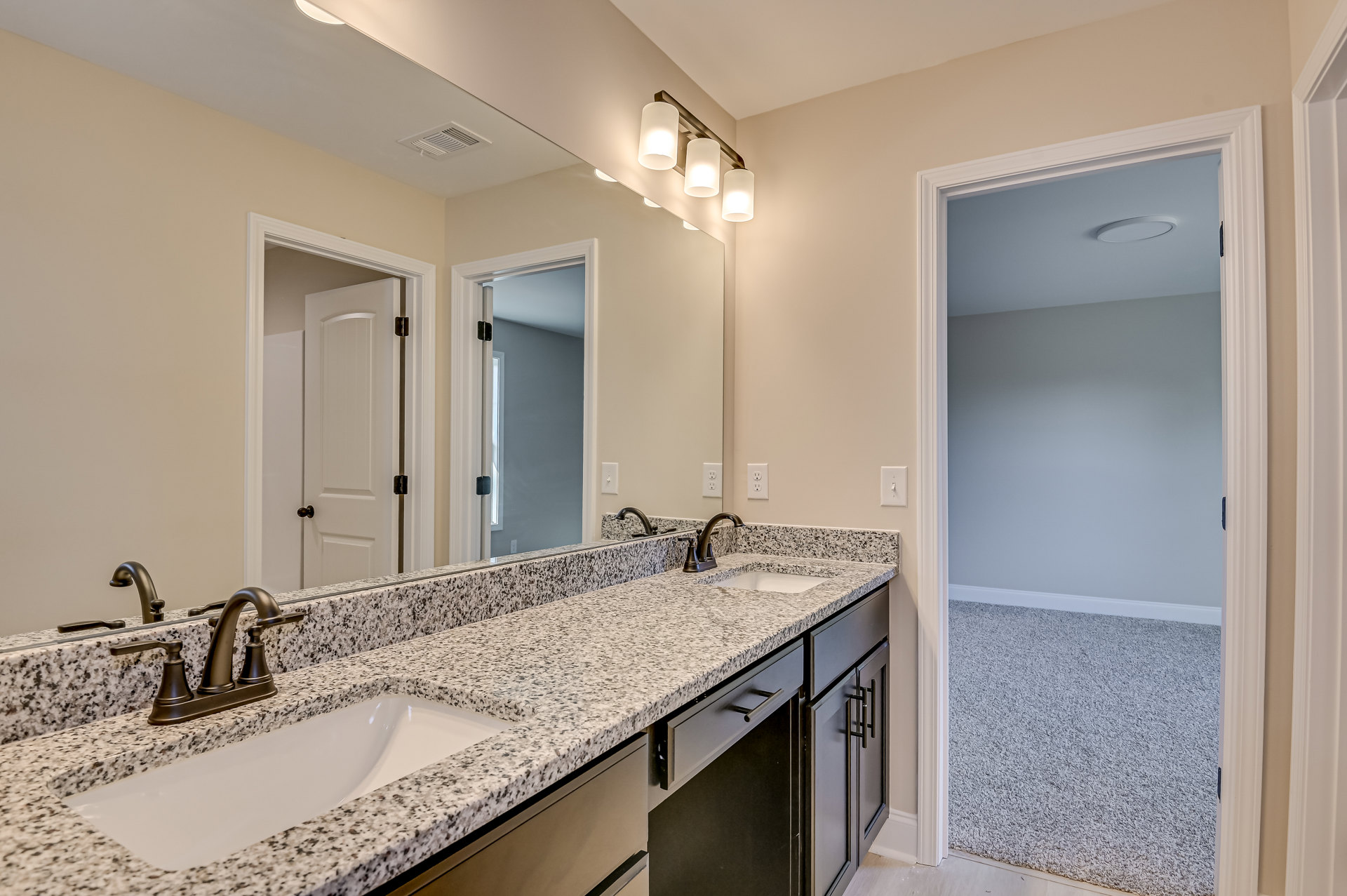 Bathroom with granite countertops, double sinks, brushed nickel faucets, three-light fixture above large mirror, white cabinetry, and neutral tile backsplash