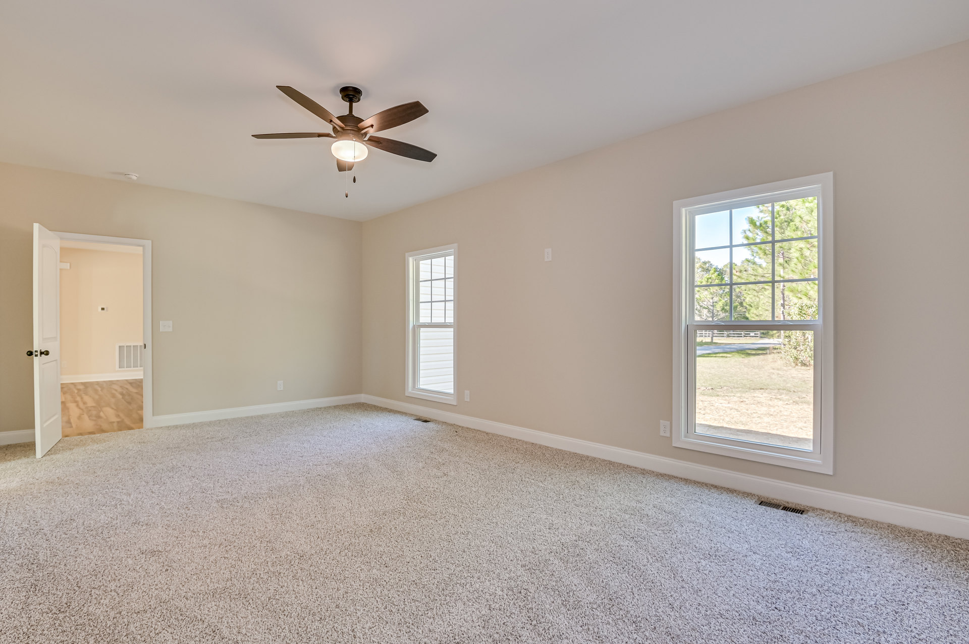 Ceiling fan with light fixture, white walls, large windows showing green trees, open white door with glass panels, wood flooring, crown molding along ceiling