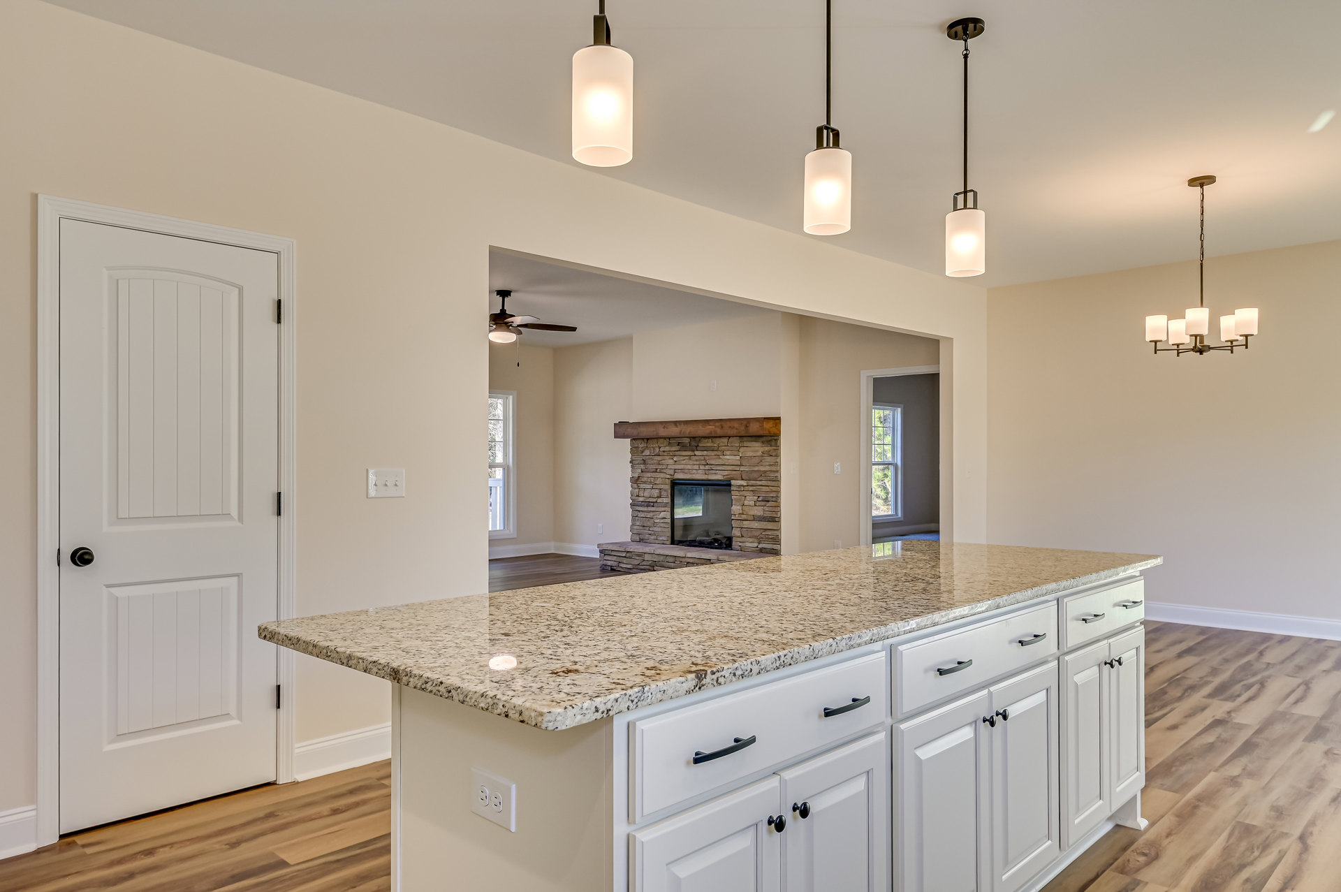 Kitchen island with white cabinets and black handles, marble countertops, rectangular pendant light, white door with black knob, fireplace featuring wood beam mantel, tile
