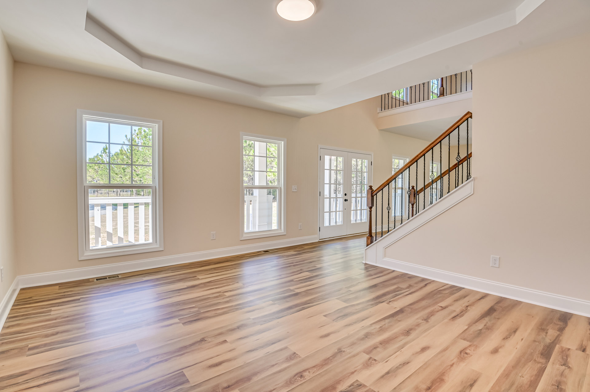 Hardwood floor room featuring a staircase with black railing, large window with white frame overlooking trees, white ceiling light, and plaster walls with molding