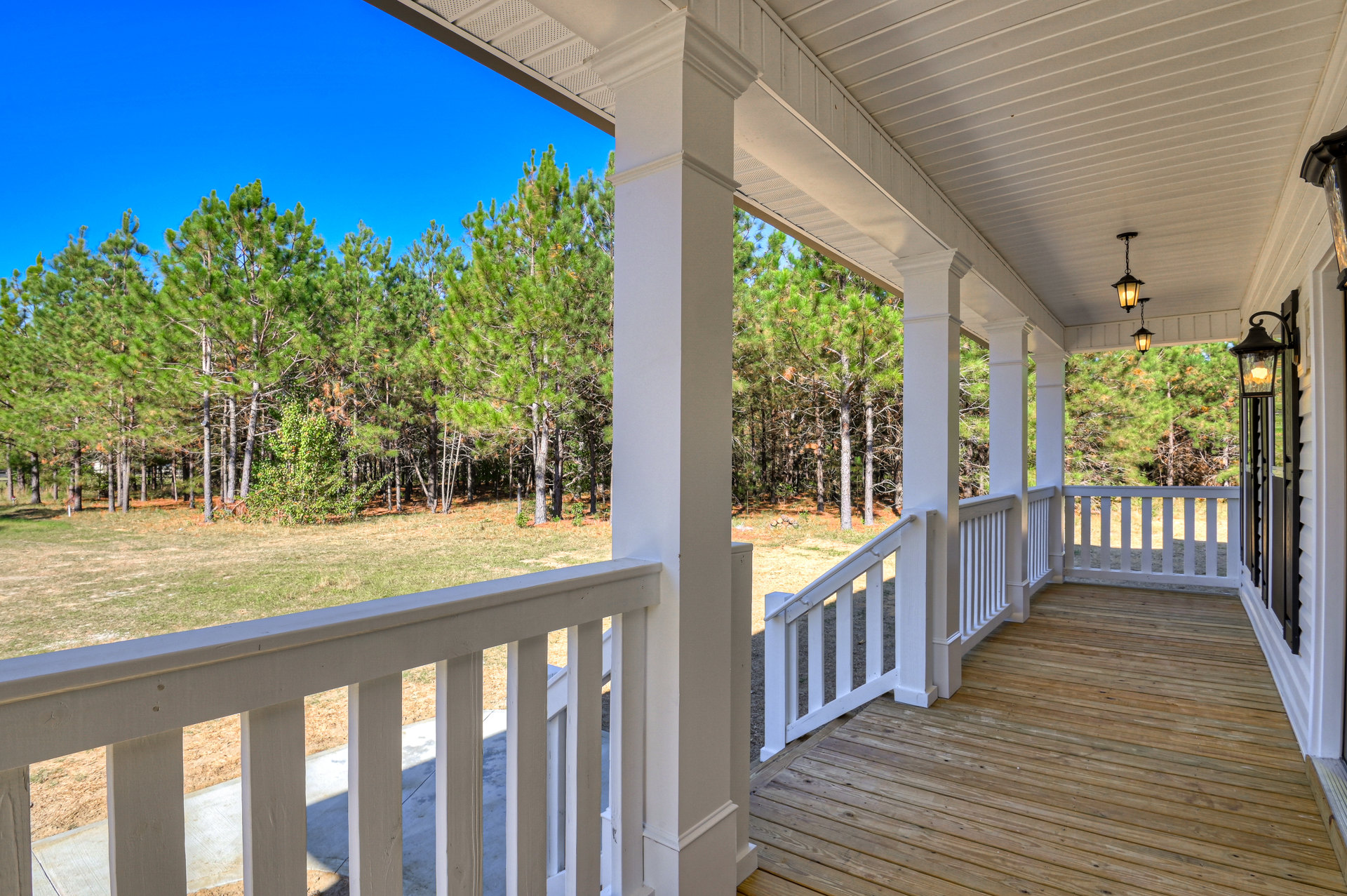 Wood deck porch with white railing, surrounded by trees, close-up window visible