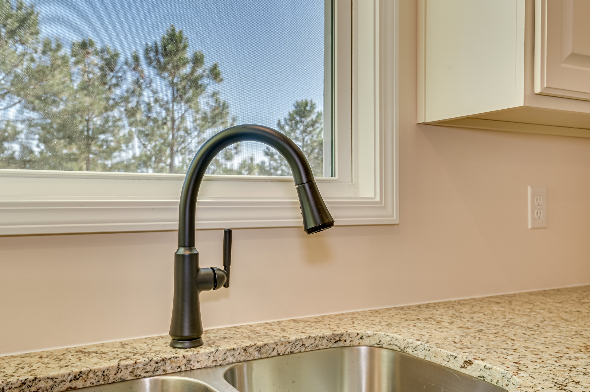 White quartz countertop with undermount stainless steel sink, matte black faucet, tile backsplash, and window overlooking green trees