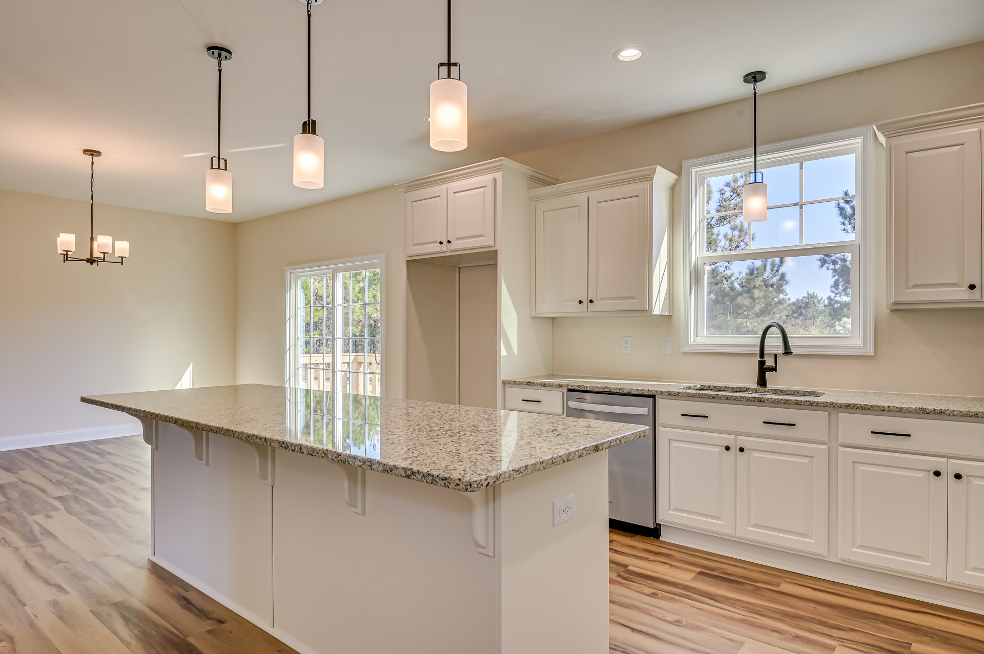 Spacious kitchen featuring a large central island with stone countertop, modern cabinetry, stainless steel sink, pendant ceiling lights, and wood flooring