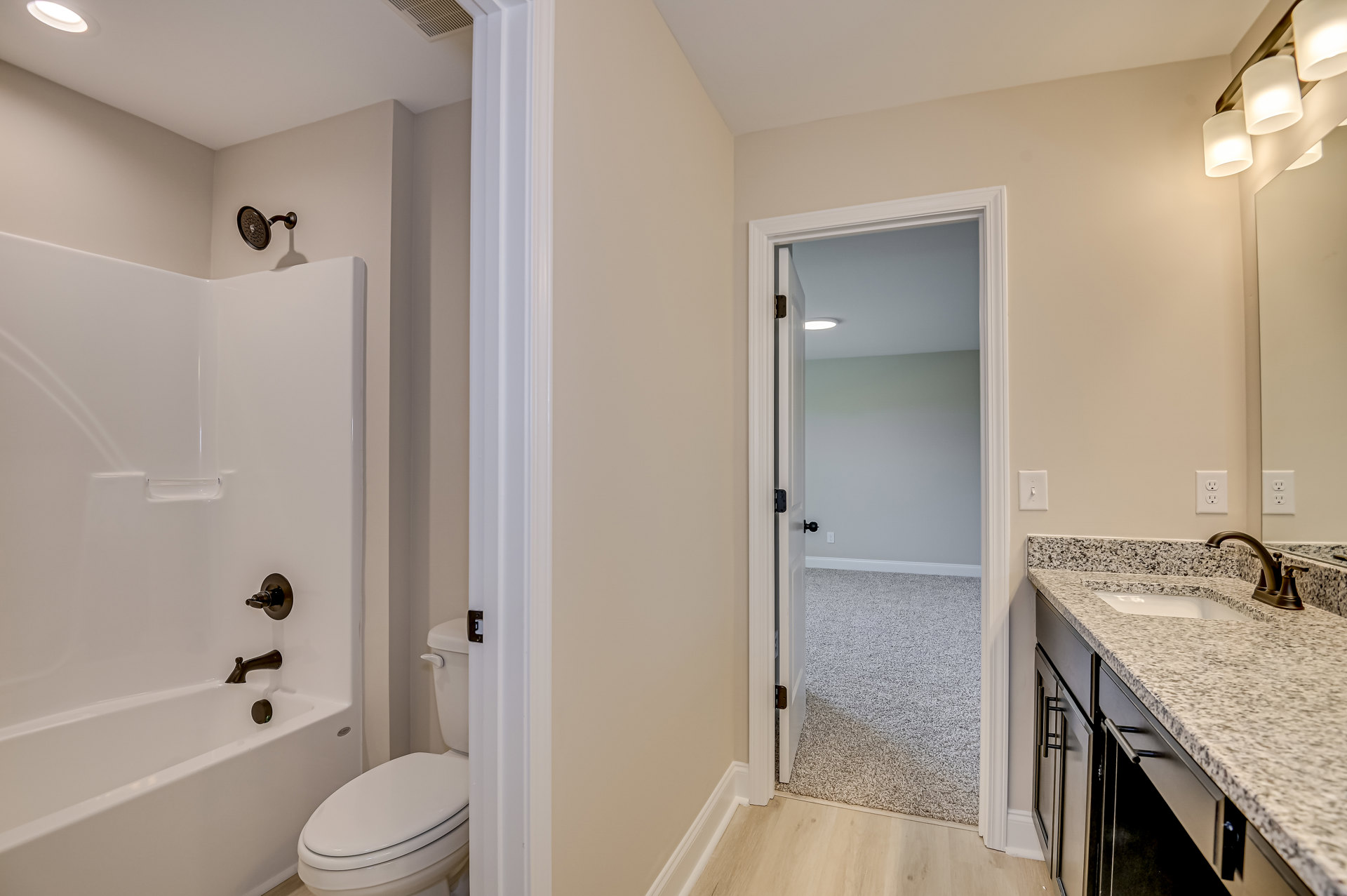 Bathroom with white tile walls, a white toilet with lid up, rectangular sink with chrome faucet, wall-mounted mirror, glass shower enclosure with round metal shower head, and