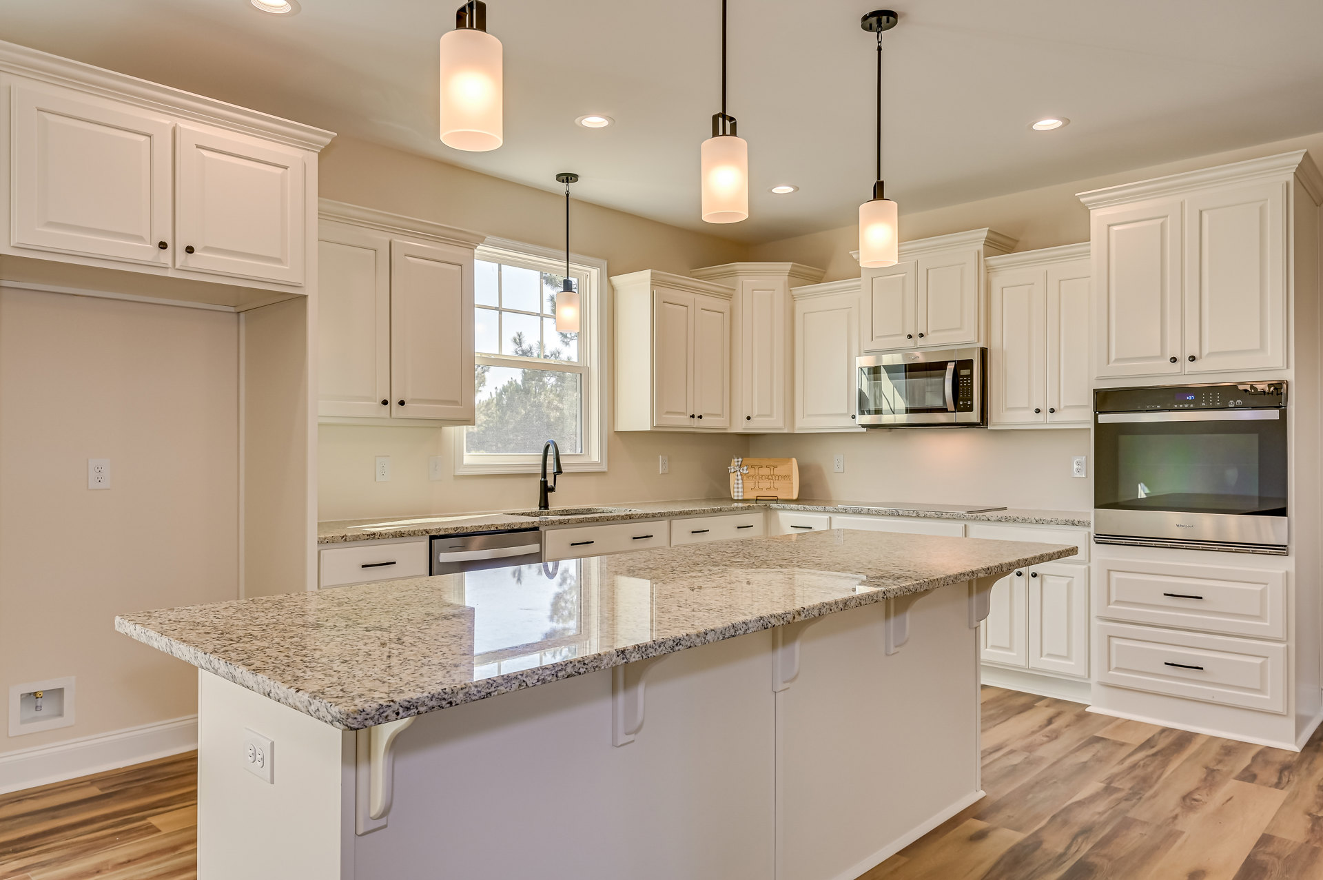 White kitchen with granite countertops, stainless steel microwave above stove, undermount sink beneath window, white cabinetry with brushed metal hardware, recessed lighting