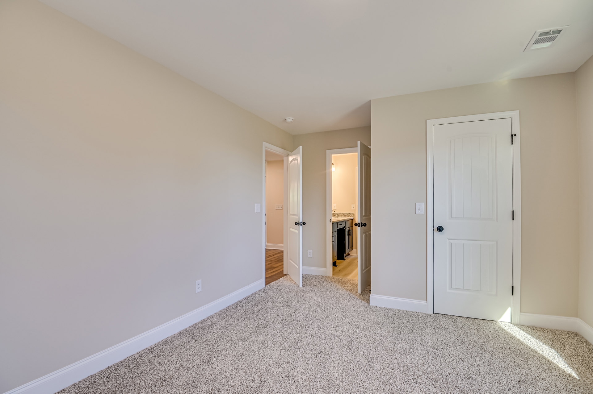White carpeted floor, white walls, open white door with black handle, ceiling vent, simple molding