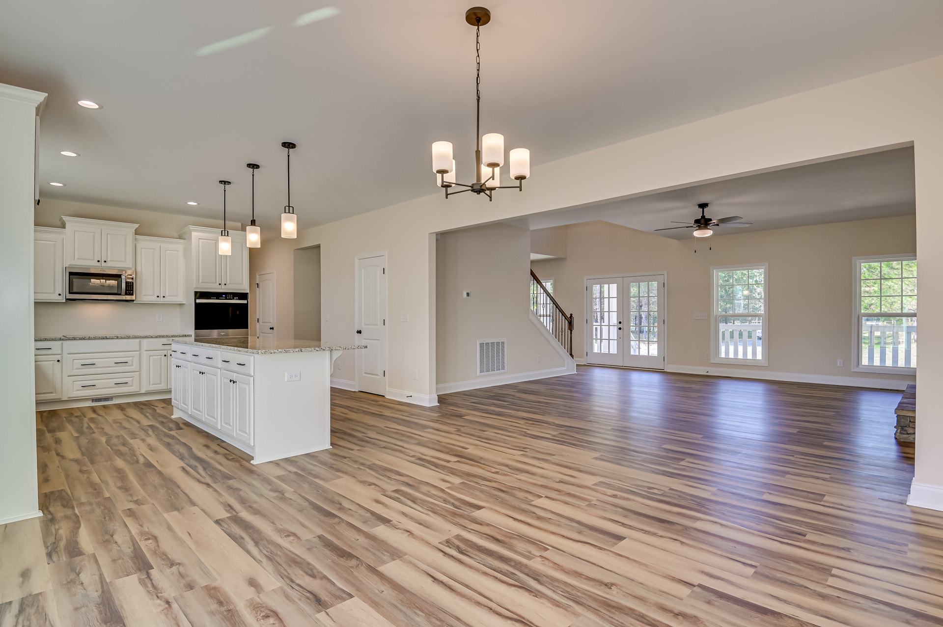 Spacious open floor plan featuring hardwood flooring, central kitchen island with cabinetry, double glass-paneled doors, white-framed windows with railings, and sticky notes on a