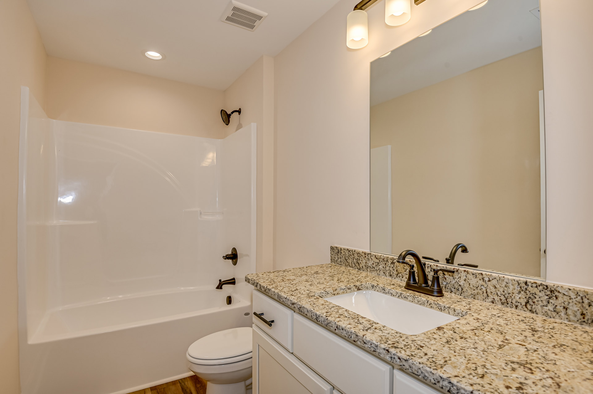 Modern bathroom featuring a wall-mounted shower head, white bathtub, and toilet, with light tile walls and chrome faucet fixtures.