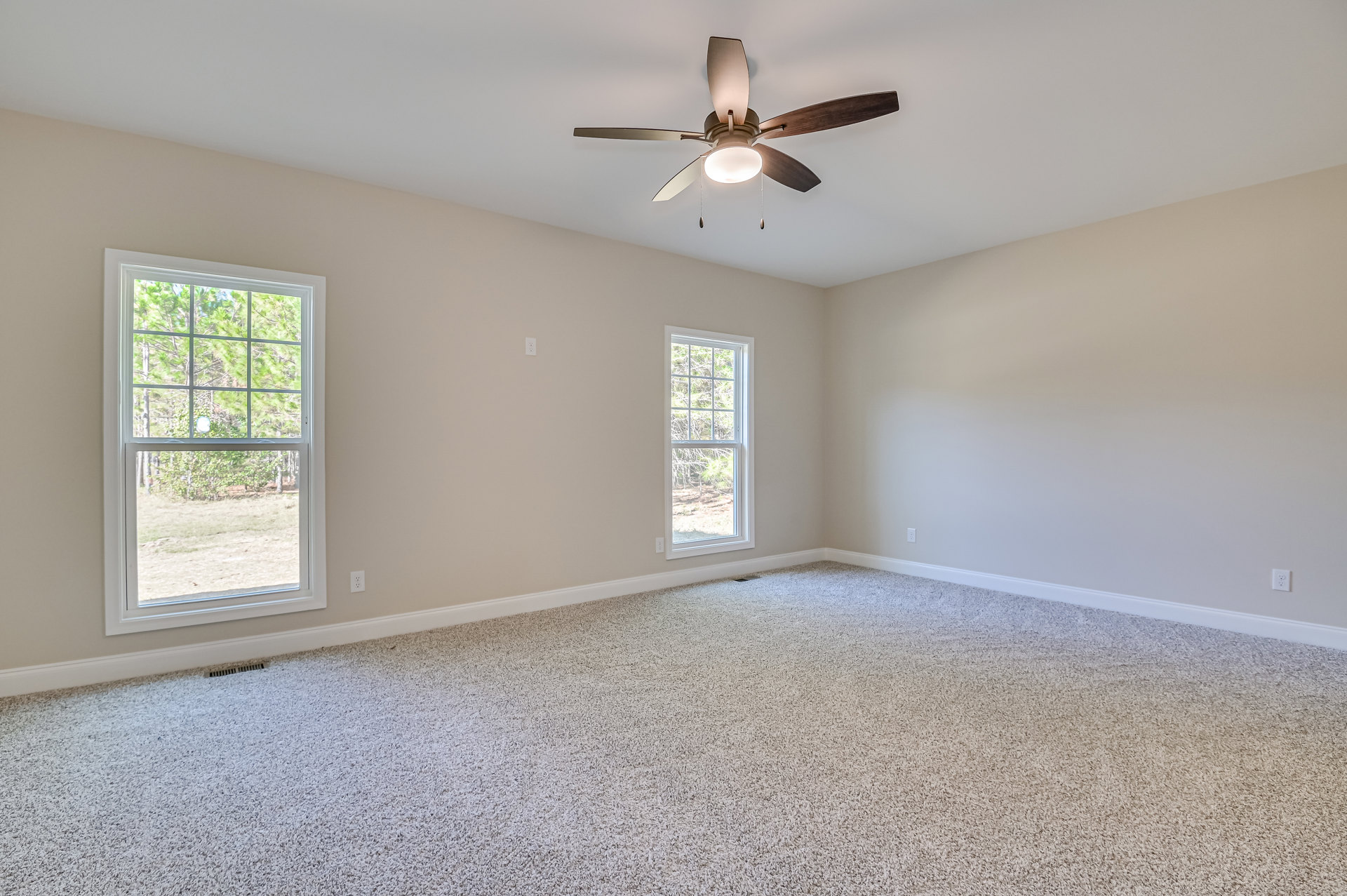 Carpeted room with white walls, ceiling fan with light fixture, multiple square windows showing green trees outside, crown molding along ceiling edges