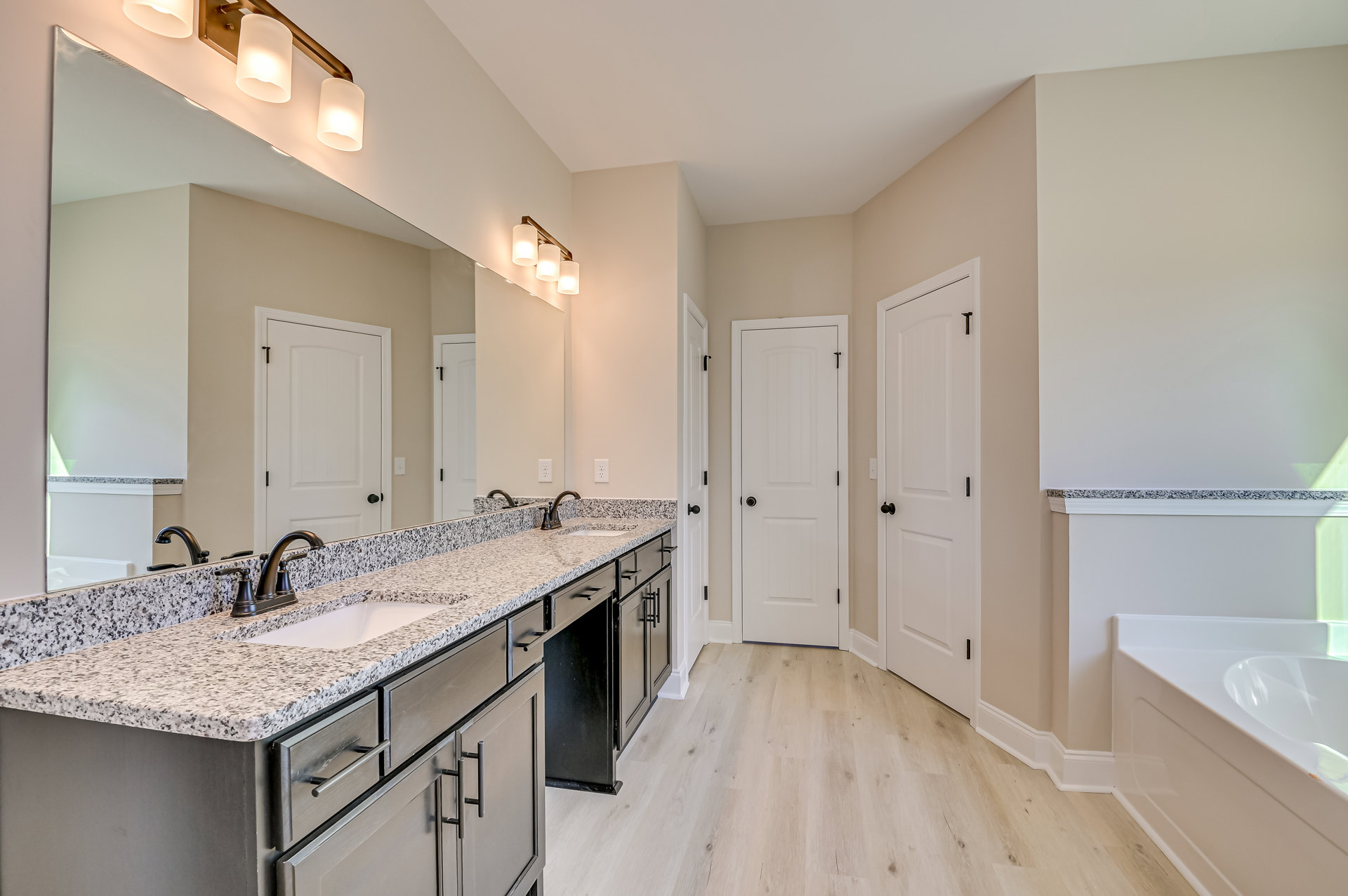 Bathroom featuring marble countertop, wood flooring, white bathtub with green lighting, wall-mounted light fixture, close-up of chrome faucet, white door with round black knob