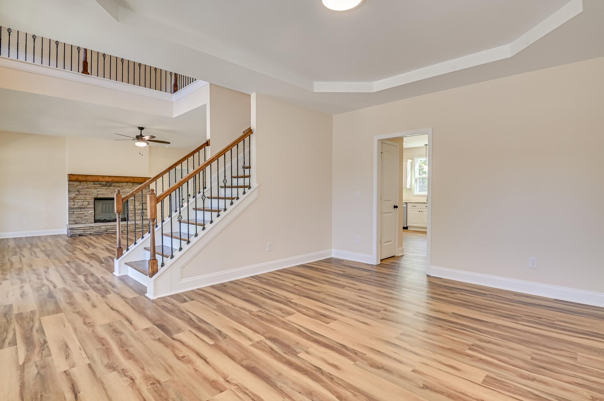 Open living area with hardwood floors, wood staircase with matching railings, stone fireplace, and ceiling fan with light fixture
