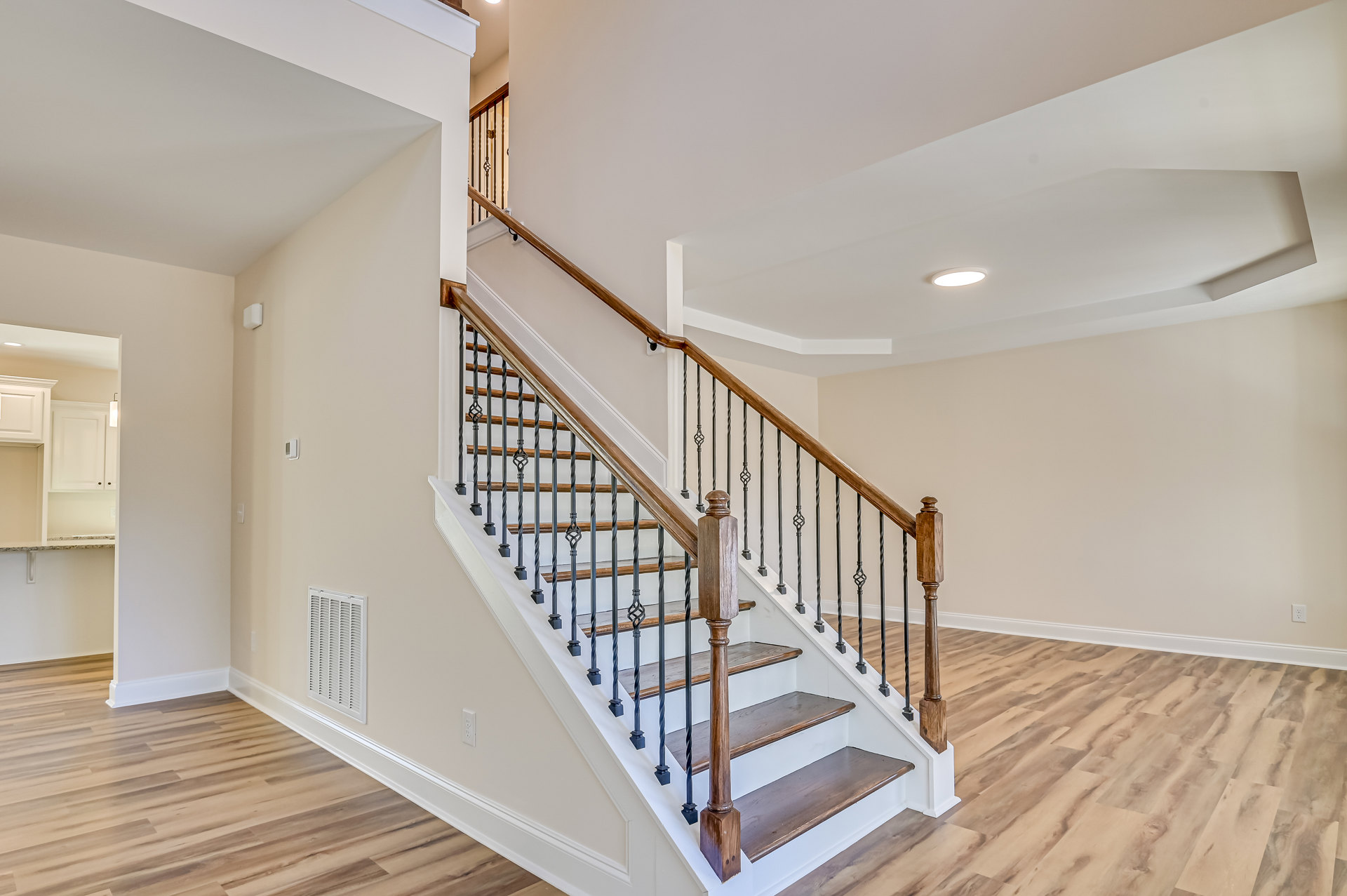 Wood staircase with matching wood railings and balusters, vent visible on plaster wall, hardwood flooring throughout interior space