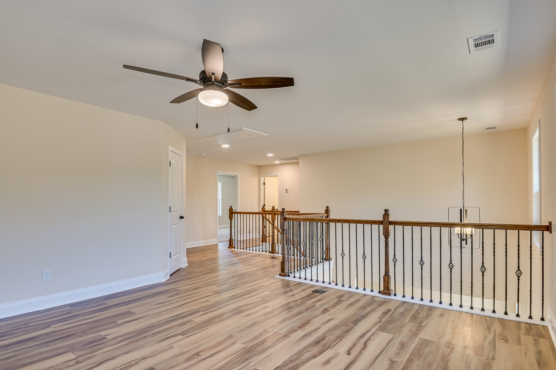 Ceiling fan with integrated light fixture mounted on white ceiling, wood flooring and wood railing, wall vent visible nearby.
